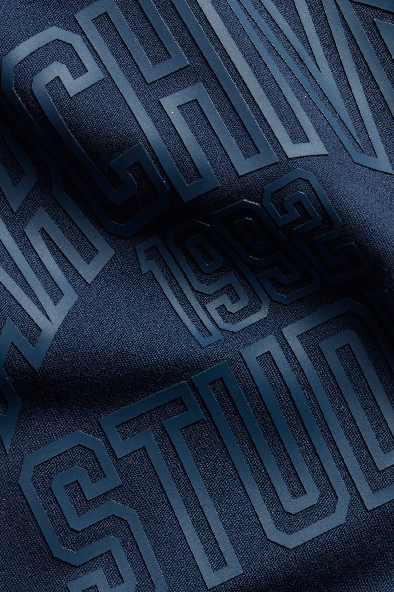 Zbliżenie na ciemnoniebieską bawełnianą bluzę z podniesionym ciemnoniebieskim nadrukiem tekstowym.