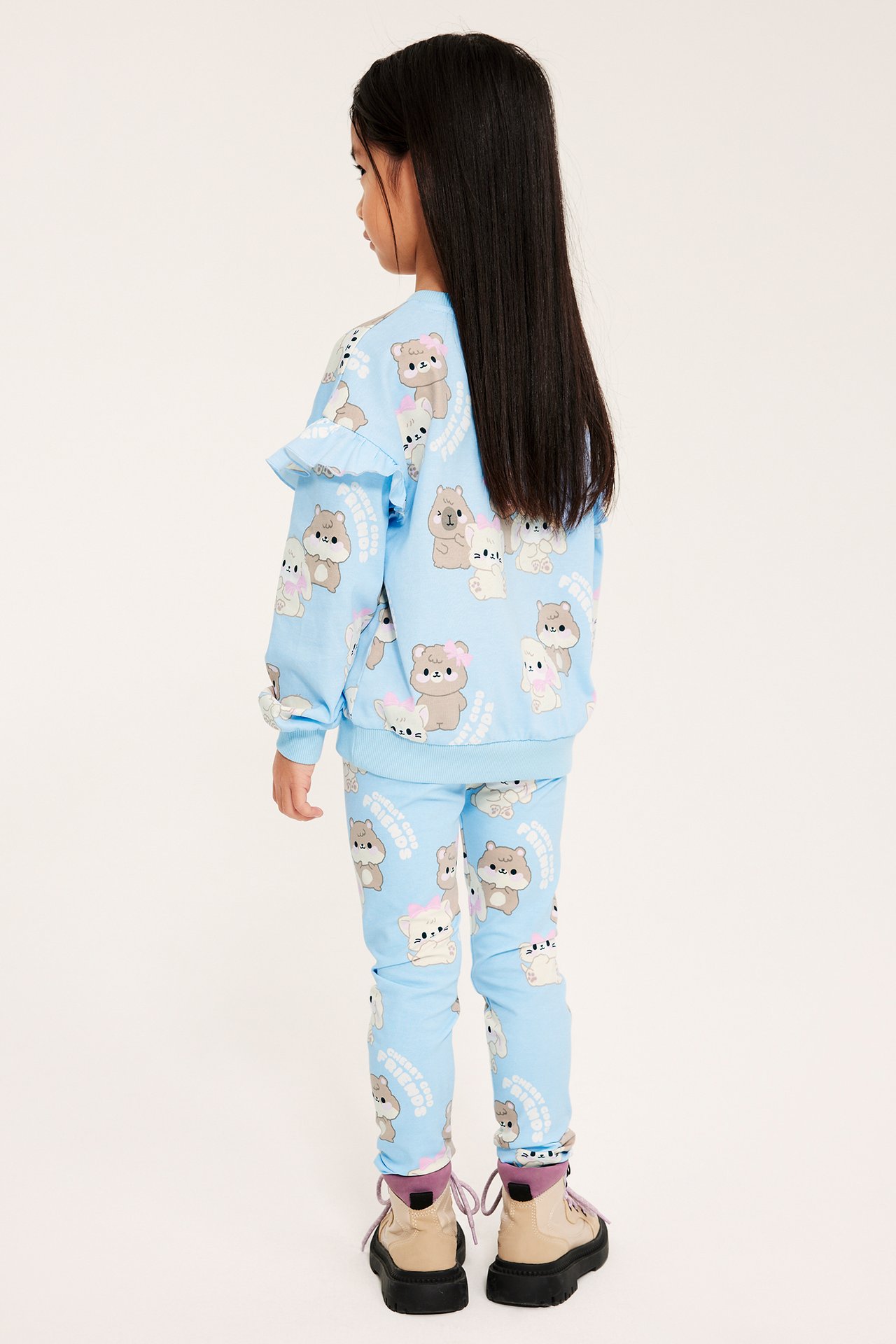 Lapsi takaa päin yllään vaaleansiniset kuviolliset leggingsit, yhteensopiva pusero ja beiget kengät.