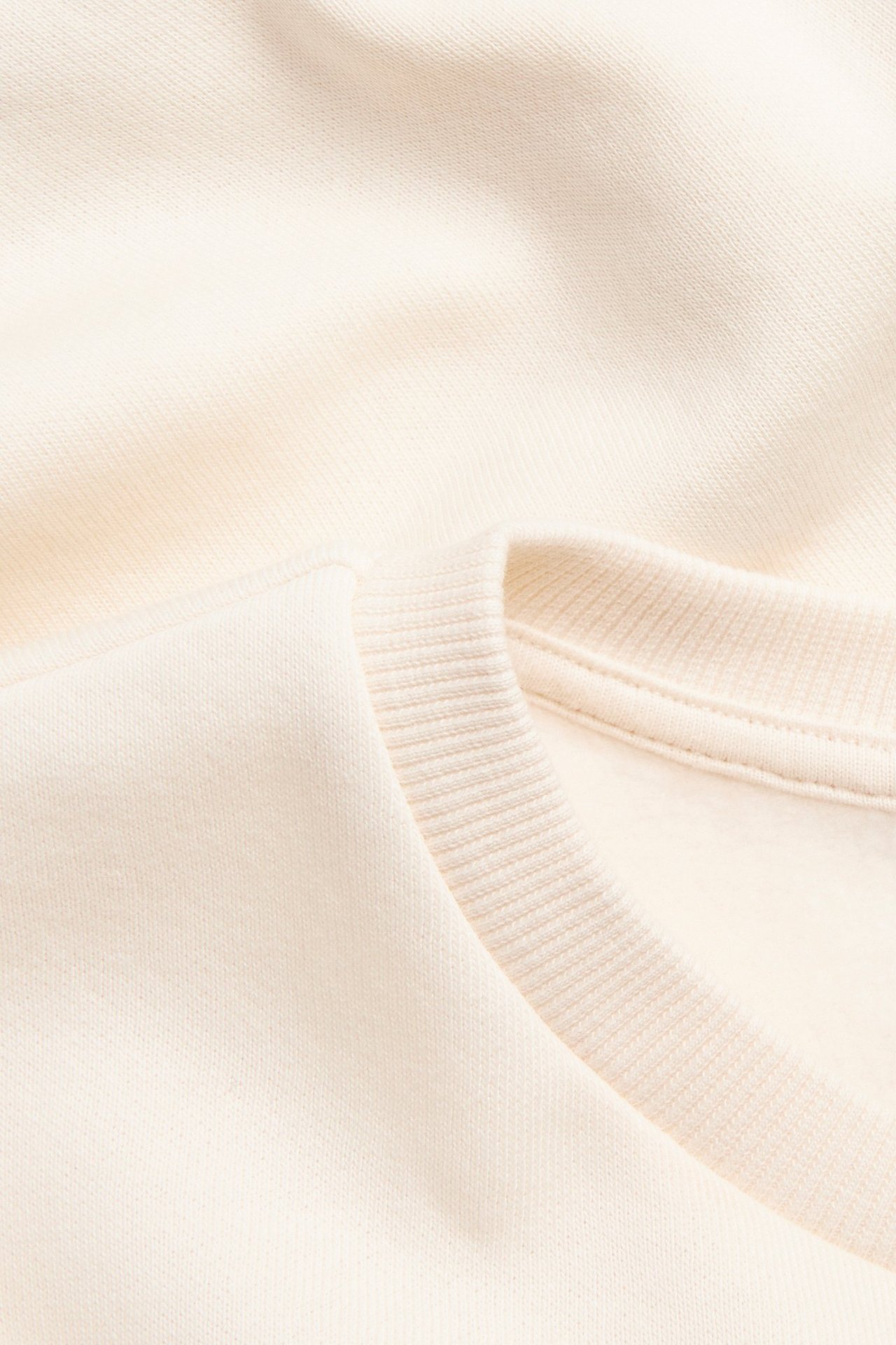 Zbliżenie na off-white bluzę dresową z miękką, szczotkowaną teksturą i prążkowanym kołnierzem.