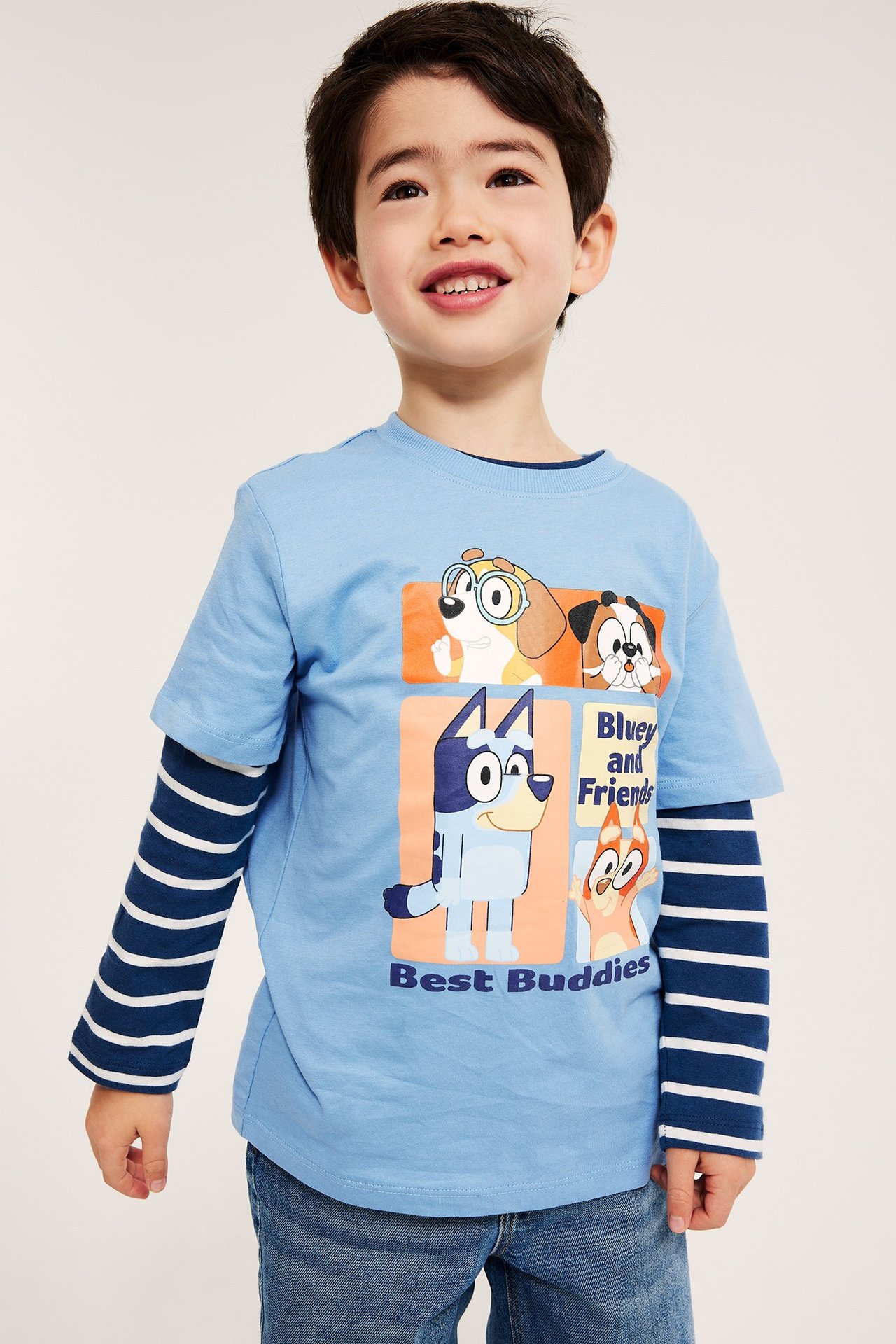 Från framsidan, ett barn i en ljusblå Bluey-mönstrad T-shirt över en randig långärmad och blå jeans.