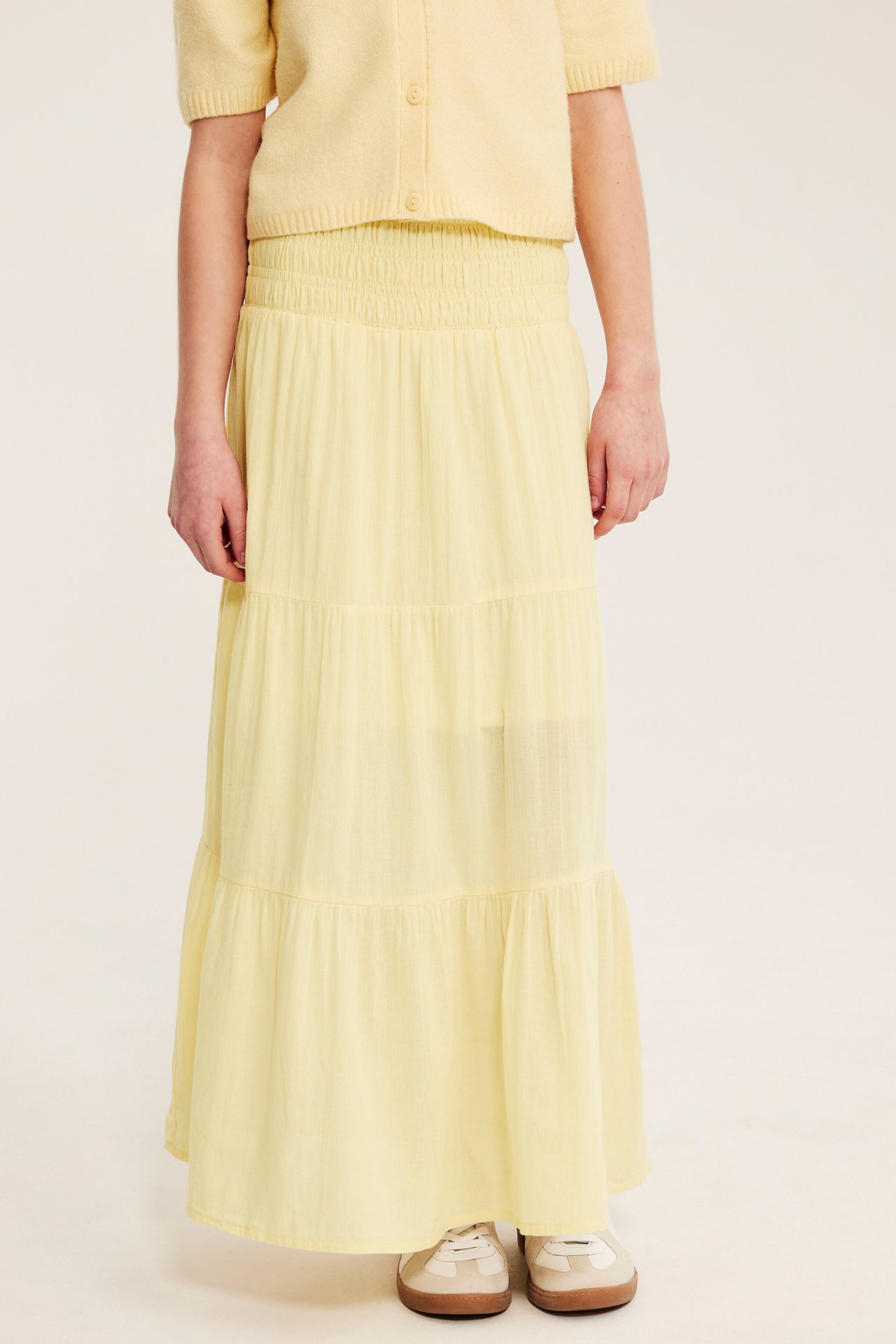 Widok z przodu: dziecko w jasnożółtej spódnicy maxi z marszczoną talią, jasnożółtym kardiganie i trampkach.