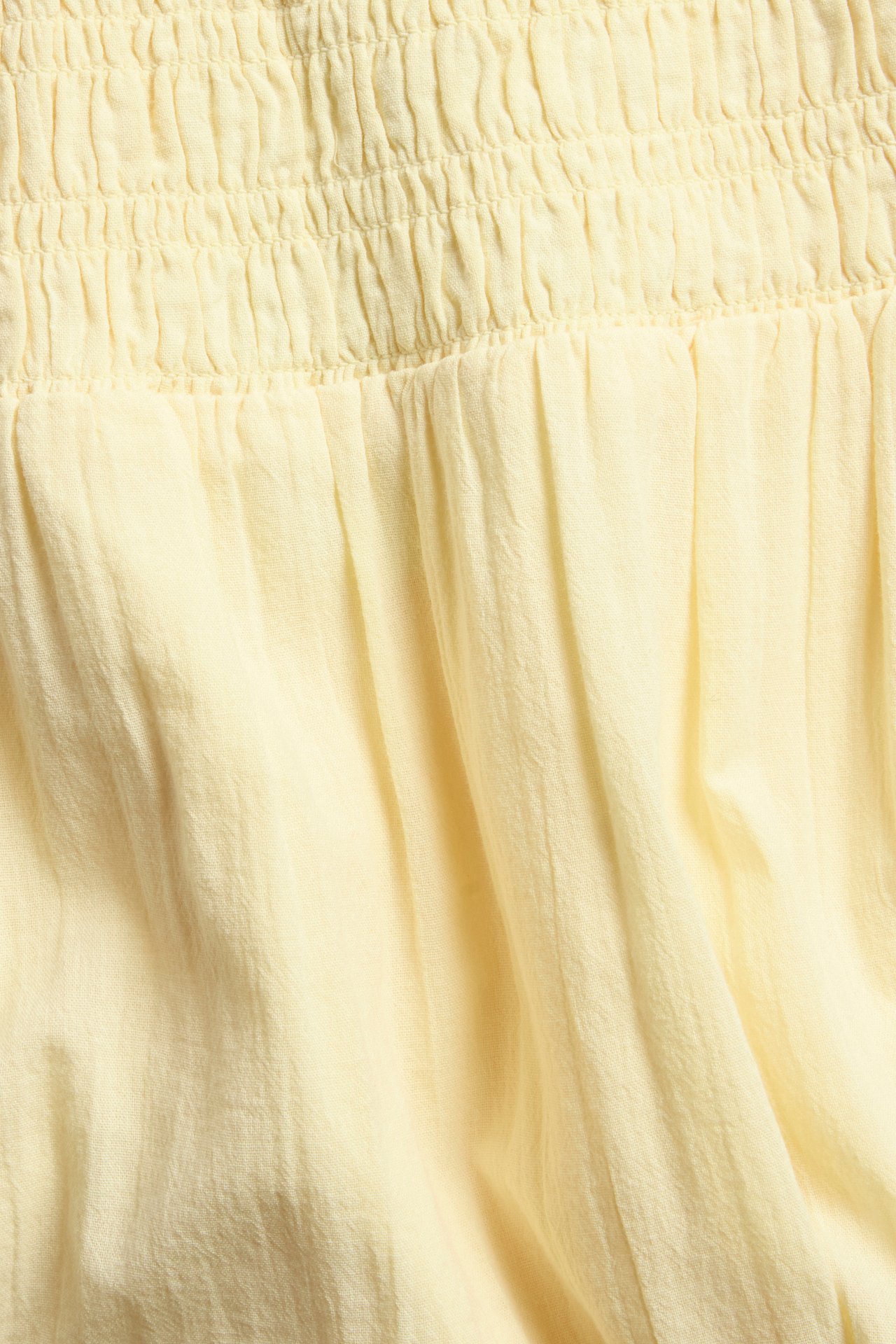Lähikuva vaaleankeltaisesta teksturoitusta puuvillamaksihameesta smokkirypytetyllä vyötäröllä.
