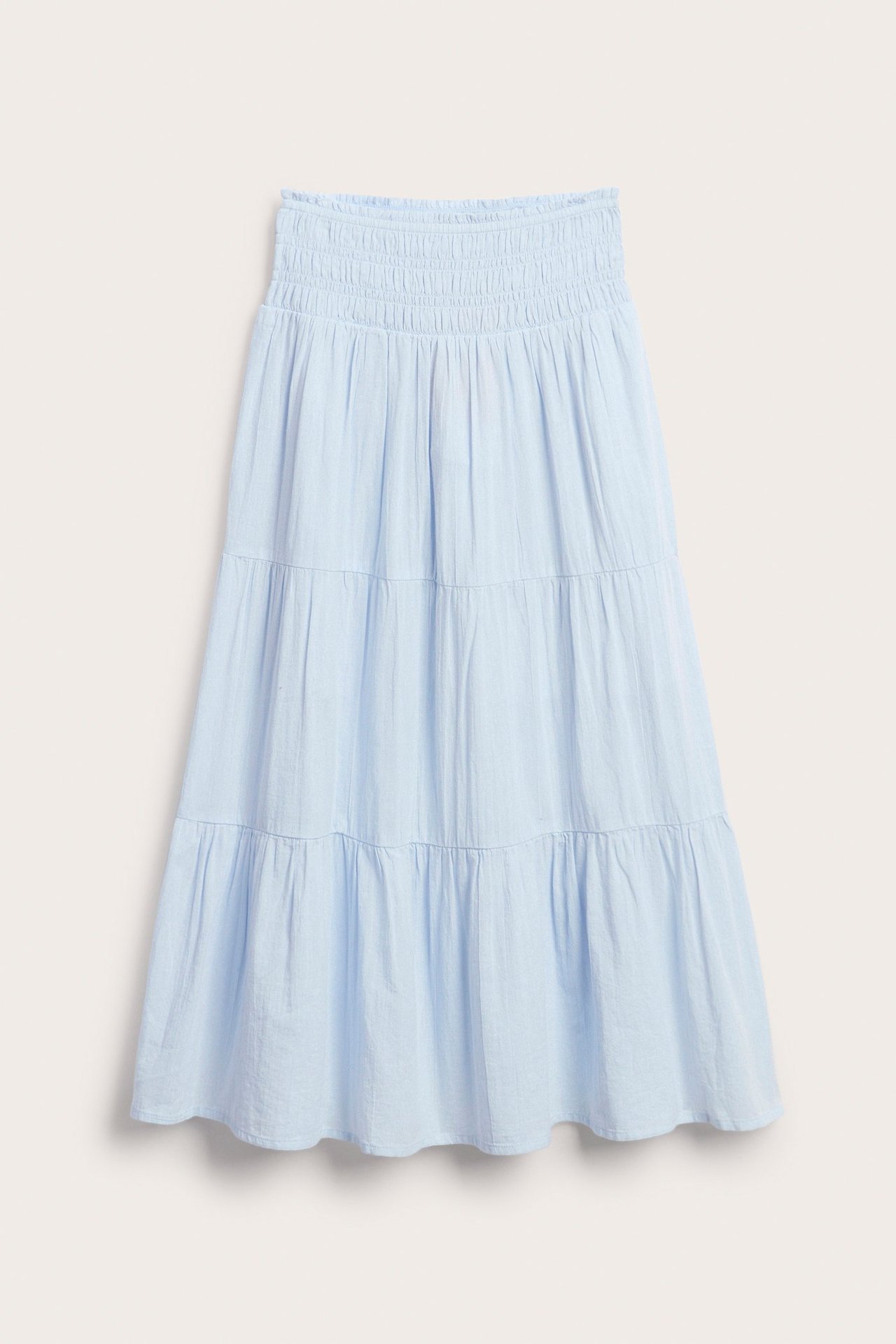 Framifrån, en ljusblå bomulls maxikjol för barn med smockad midja och volanger i lager.