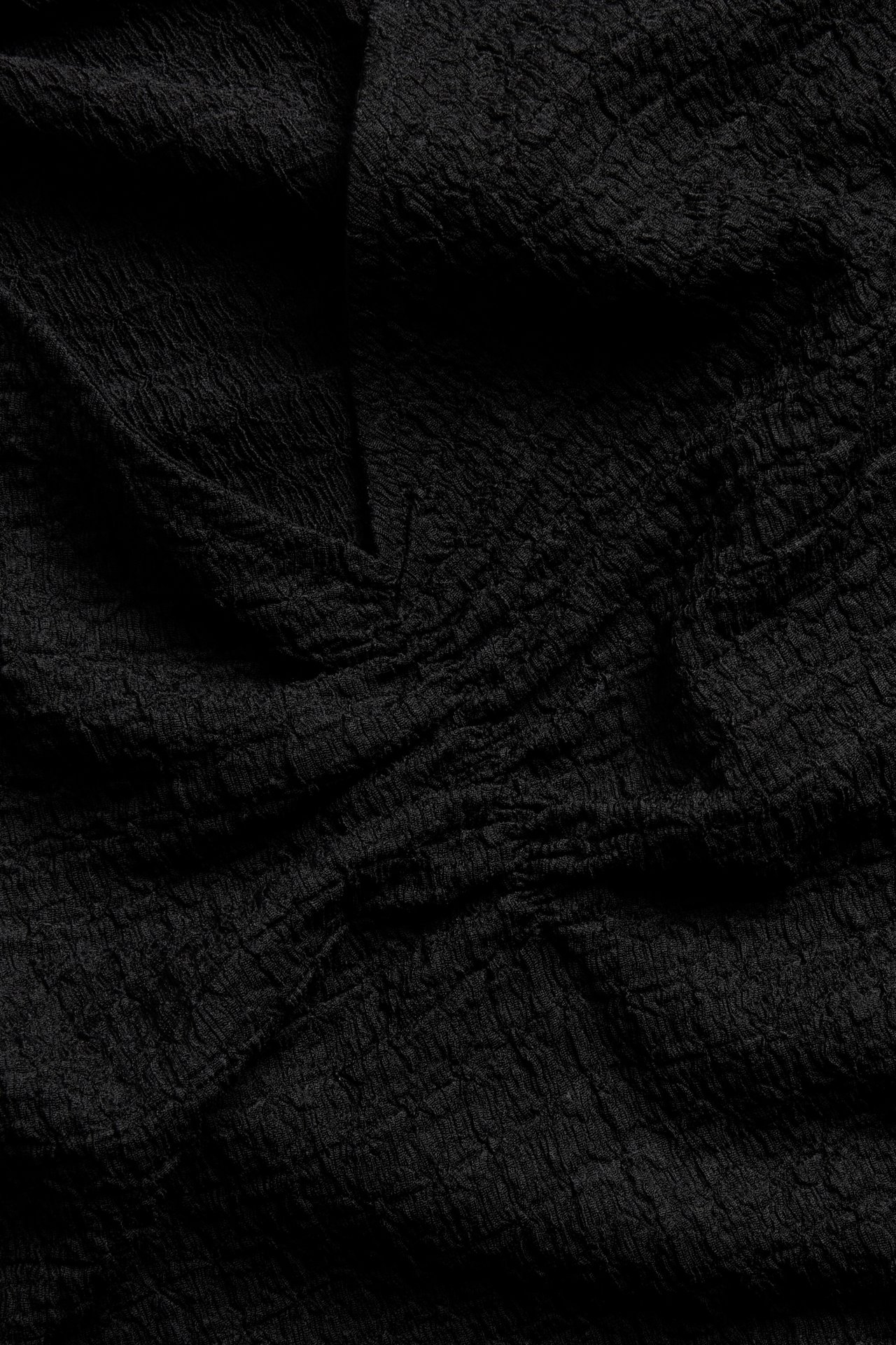 Nærbilde av en svart strukturert topp's polyester- og elastanstoff, som viser dens krøllete overflate.