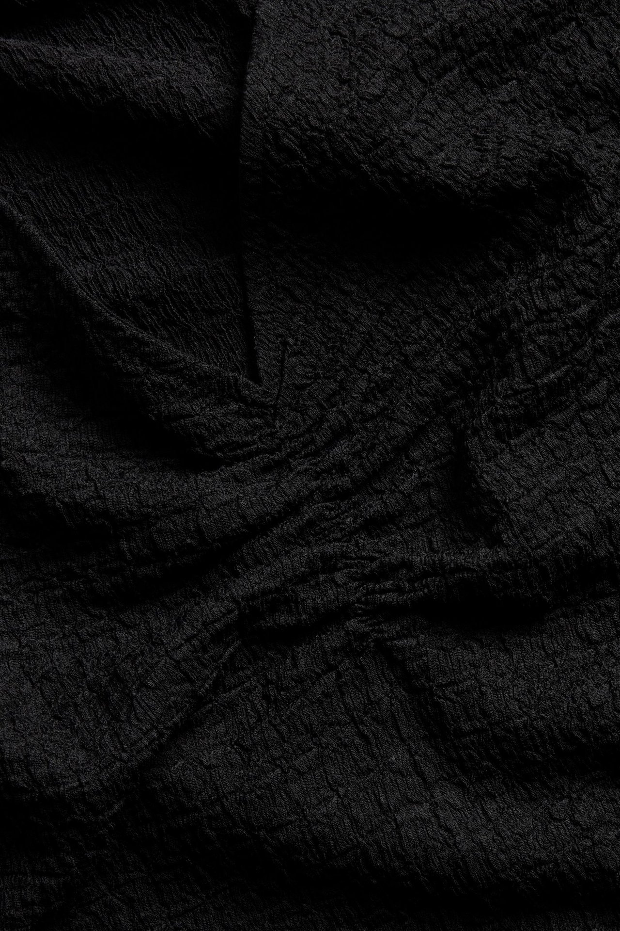 Lähikuva mustan kuvioidun topin polyesteri- ja elastaanikankaasta, näyttäen sen rypytetyn pinnan.
