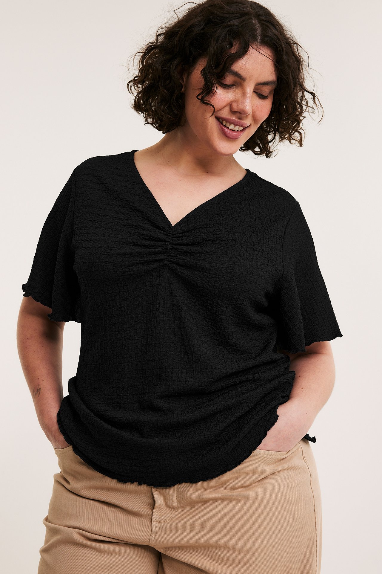 Svart texturerad V-ringad topp med utsvängda ärmar och rynkad front. Bärs med beiga byxor.