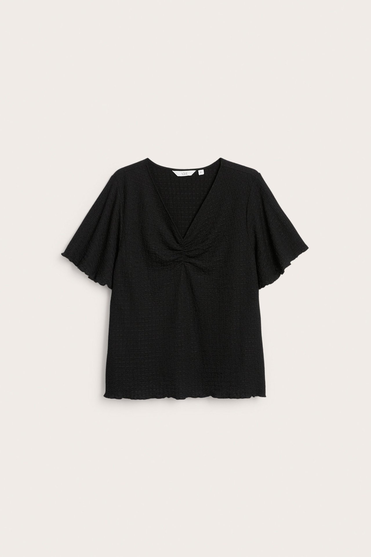 Edestä näkymä mustasta lyhythihaisesta V-aukkoisesta topista, jossa on kuvioitu kangas, rypytetty yksityiskohta ja aaltoilevat reunat.