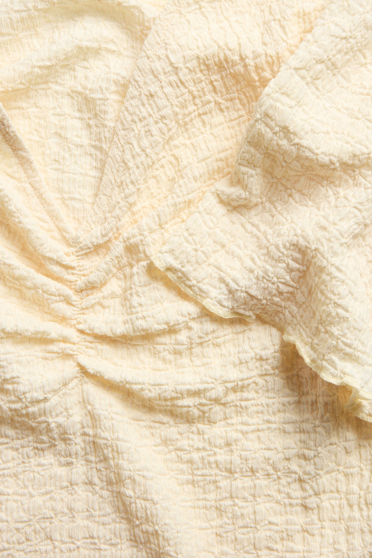 Nærbilde av en lys gul strukturert topp med rynkede detaljer foran.