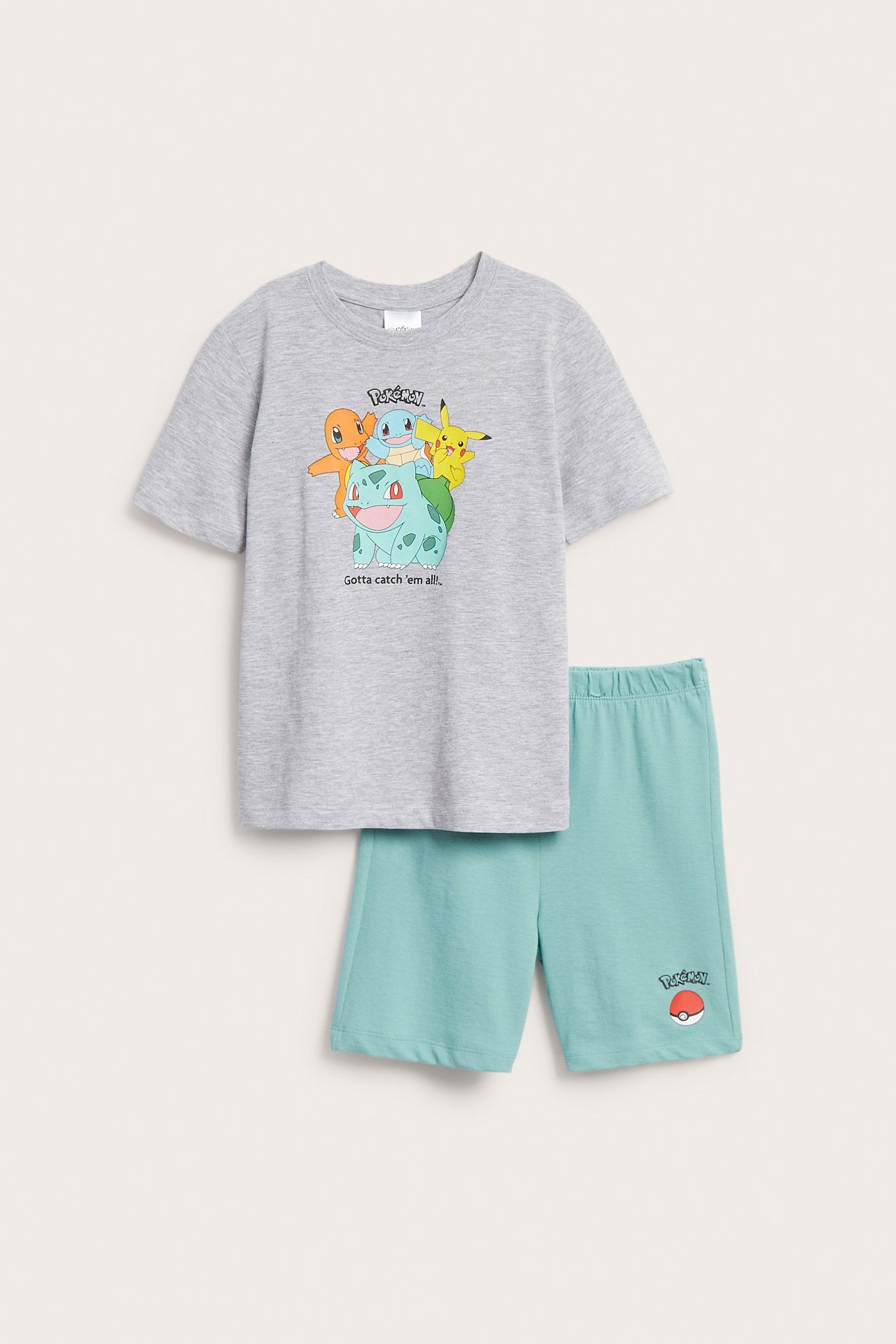 Framifrån, pyjamas för barn: grå kortärmad bomullstopp med Pokémon-tryck och turkosa bomullsshorts.