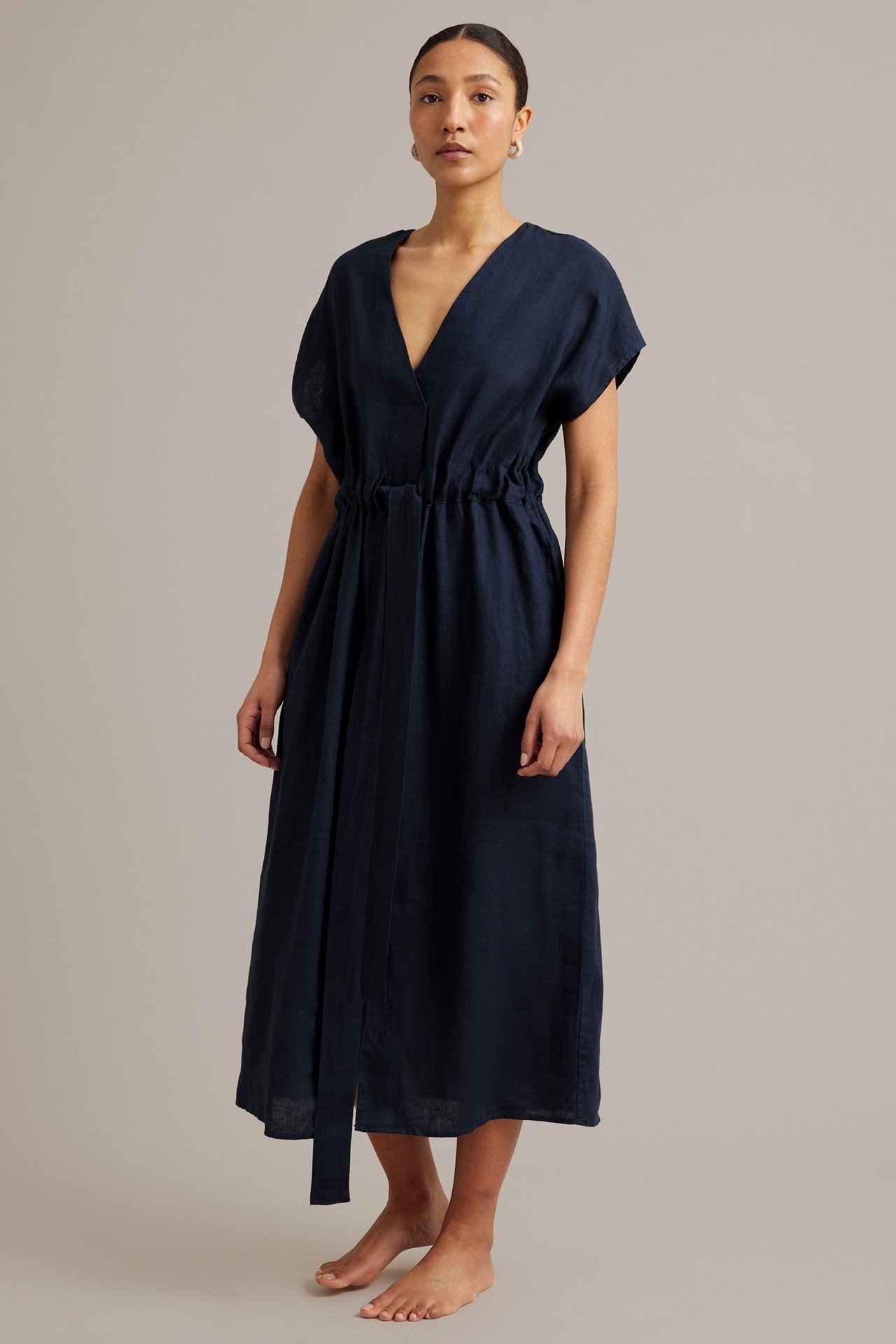 Framifrån: kvinna i mörkblå linneklänning med V-ringning och resårlinning med knytband i midjan.