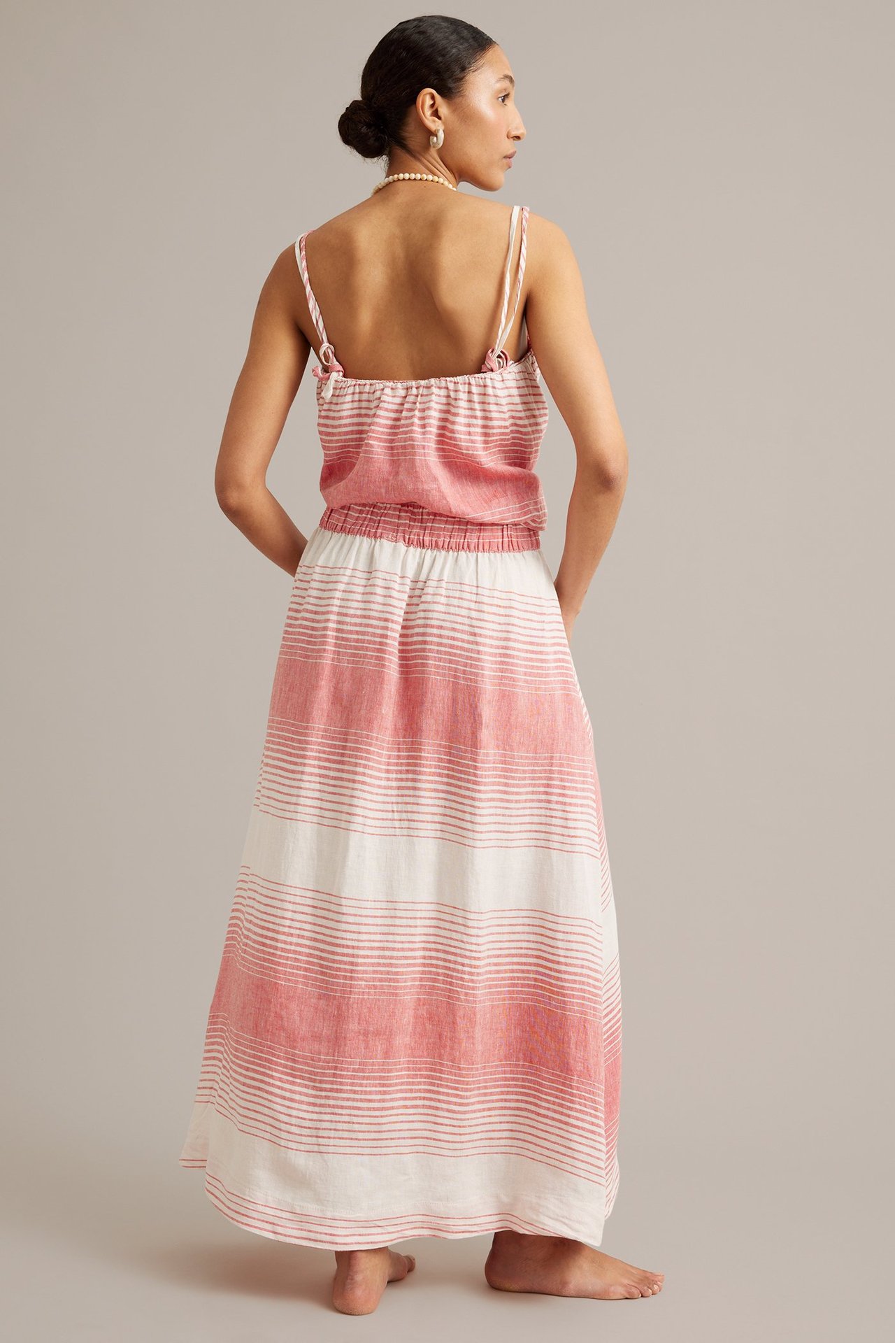 Ryggvy: kvinna i lång röd- och vitrandig linnekjol, matchande camisoletop, pärlhalsband.