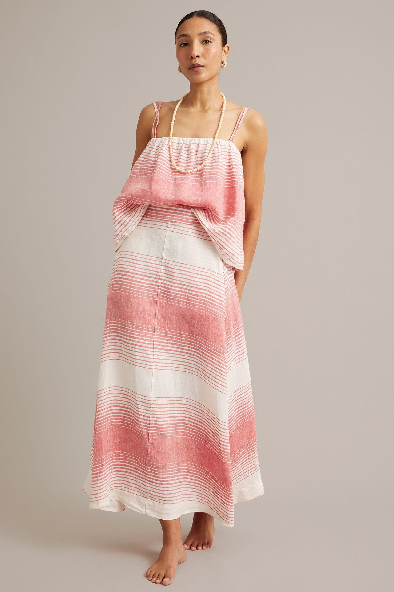 Frontvy: Kvinna i lång rödvitrandig linnekjol, matchande linne, och ett pärlhalsband.