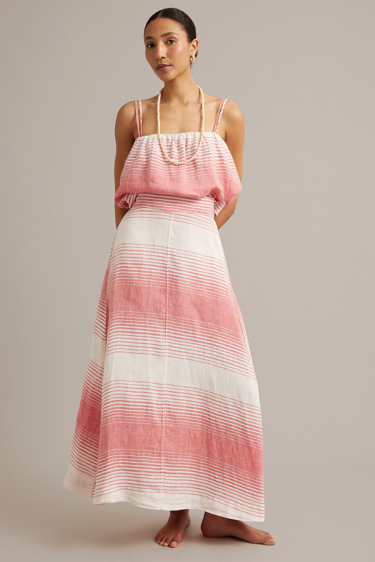 Frontvy av en kvinna i en rödvitrandig maxikjol i linne, matchande topp och pärlhalsband.