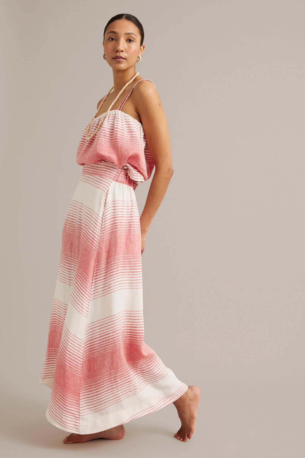 Sidovy av kvinna i lång rödvitrandig linnekjol, matchande camisole, pärlhalsband och örhängen.