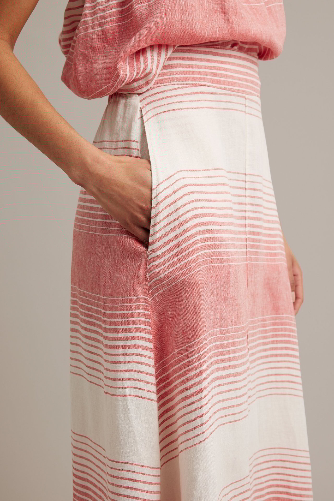 Närbild sidovy: kvinnas hand i fickan på röd- och vitrandig linnekjol och matchande topp.