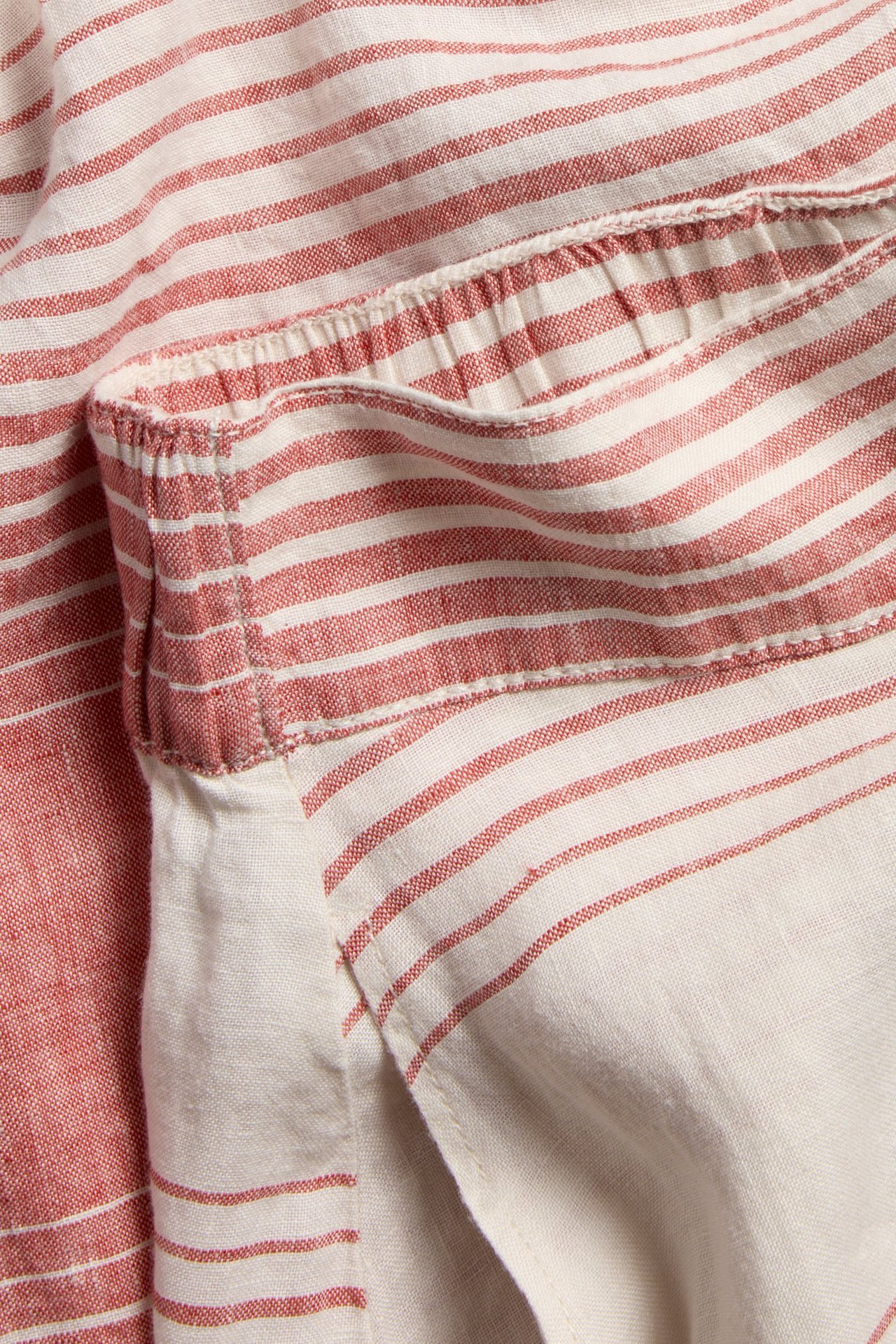 Närbild på en röd- och benvitrandig linnekjol med resårlinning och sidoficka.