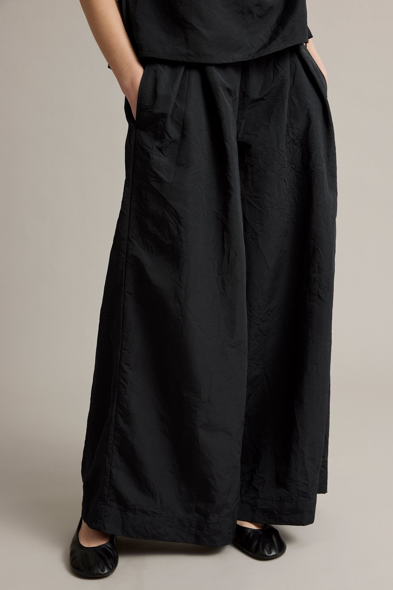 Kvinna i svarta texturerade vida byxor, matchande topp och svarta ballerinaskor, frontvy.