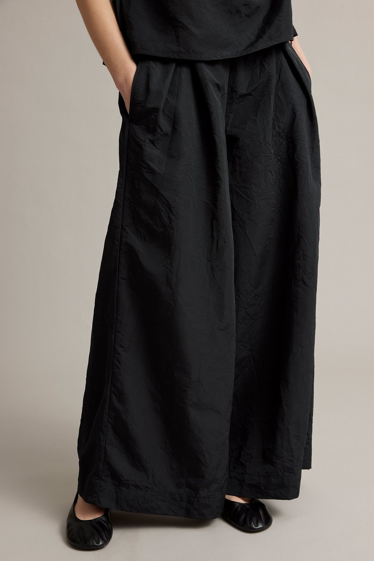 Kvinne i svarte teksturerte vide bukser, matchende topp og svarte flate sko, frontvisning.