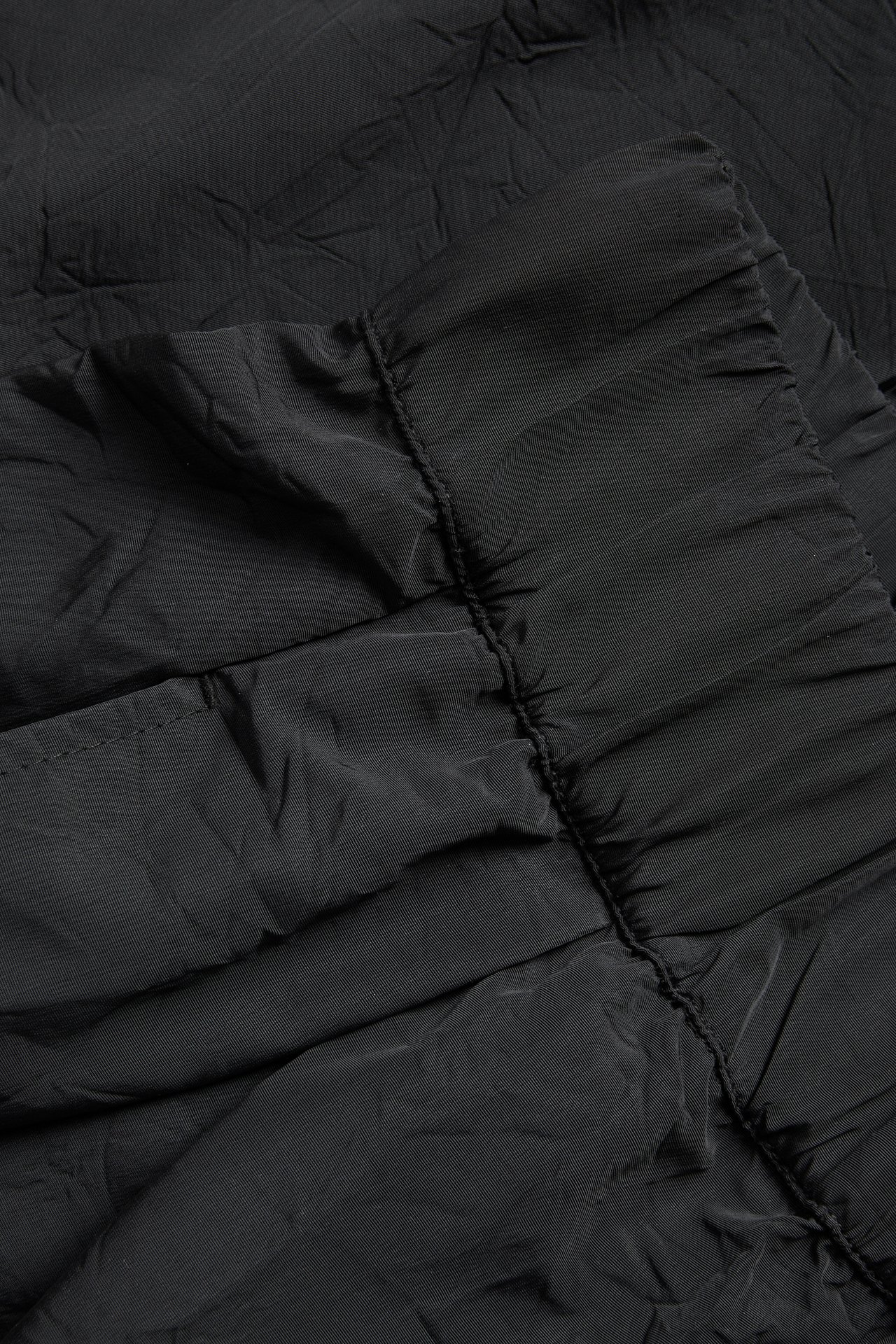 Nærbilde av svarte vide bukser i teksturert polyesterstoff med synlige rynker.