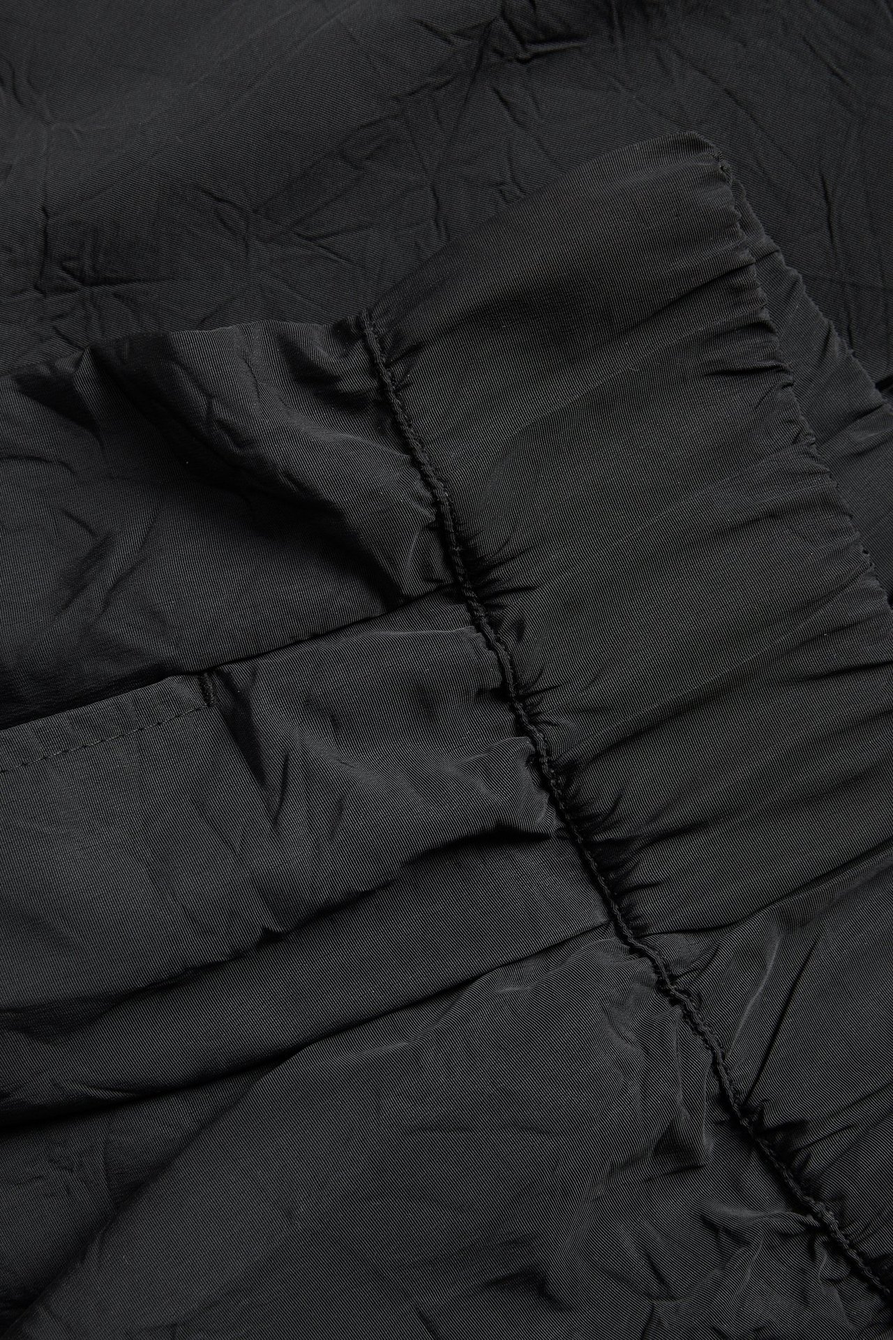 Nærbilde av svarte vide bukser i teksturert polyesterstoff med synlige rynker.