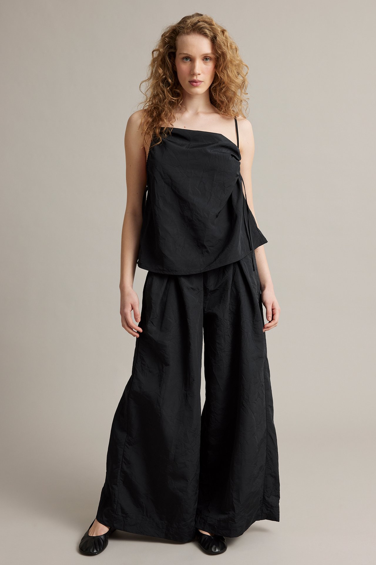 Widok z przodu kobiety w czarnych szerokich spodniach ze strukturalnej tkaniny, czarnej koszulce i balerinkach.