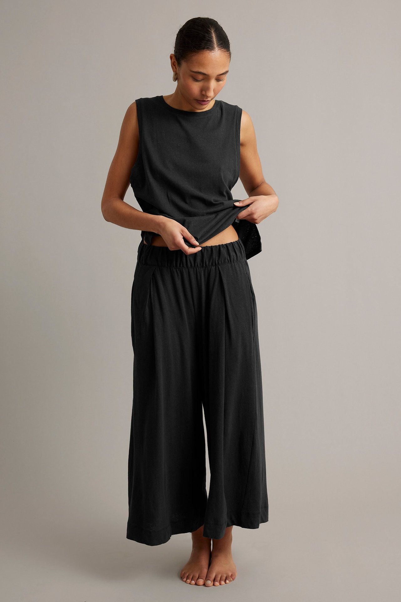 Helfigur framifrån, kvinna i svarta culottebyxor i bomull/linne med veck och matchande svart ärmlös topp.