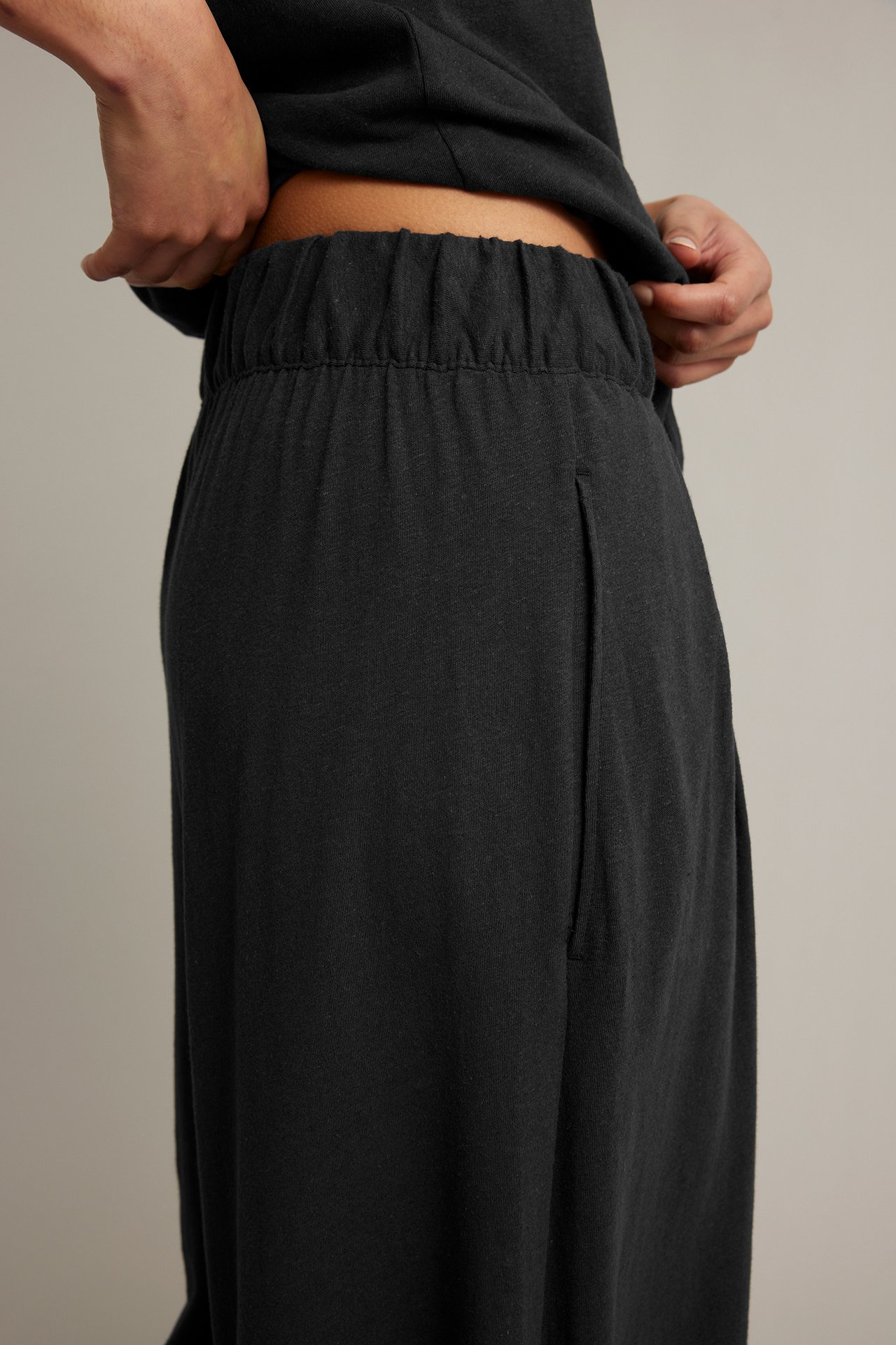 Närbild sidovy: kvinna i svarta culottebyxor i bomullslinne med resårlinning, sidfickor, och svart topp.