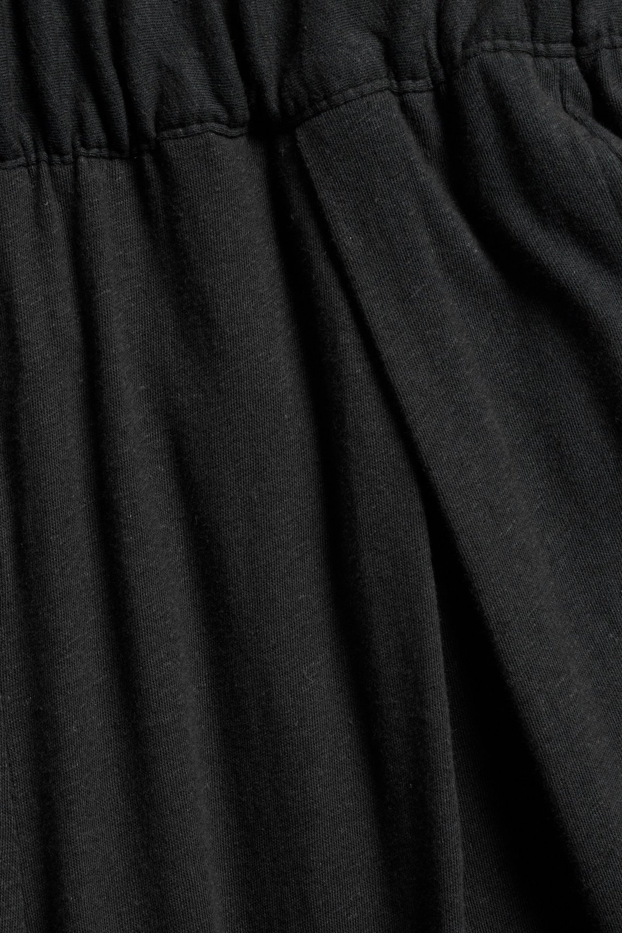 Närbild av svarta culottebyxor i bomull-linneblandning med resår i midjan och lagda veck fram.