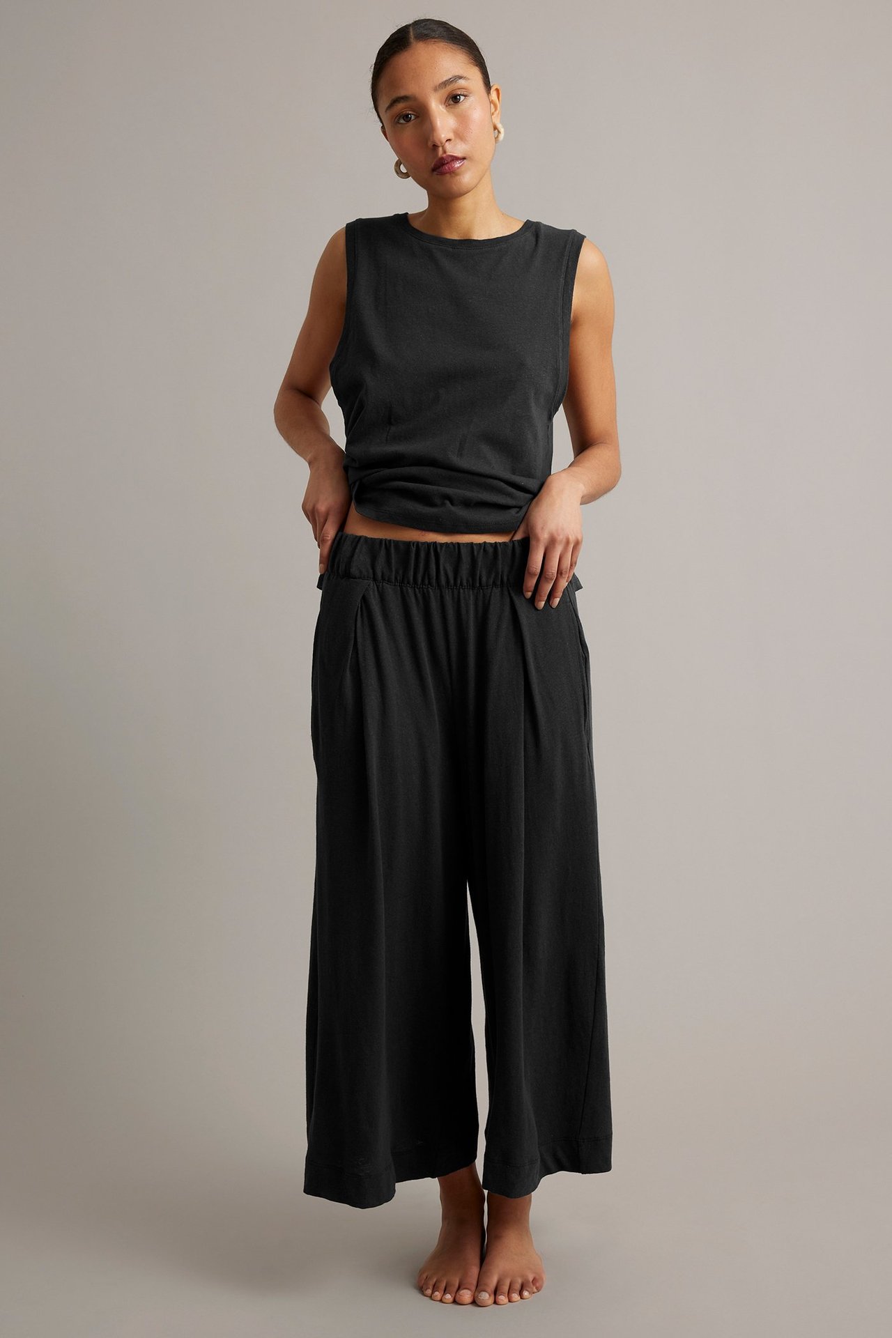 Widok z przodu: kobieta w czarnych, szerokich kulotach z zakładkami i pasującym topie.