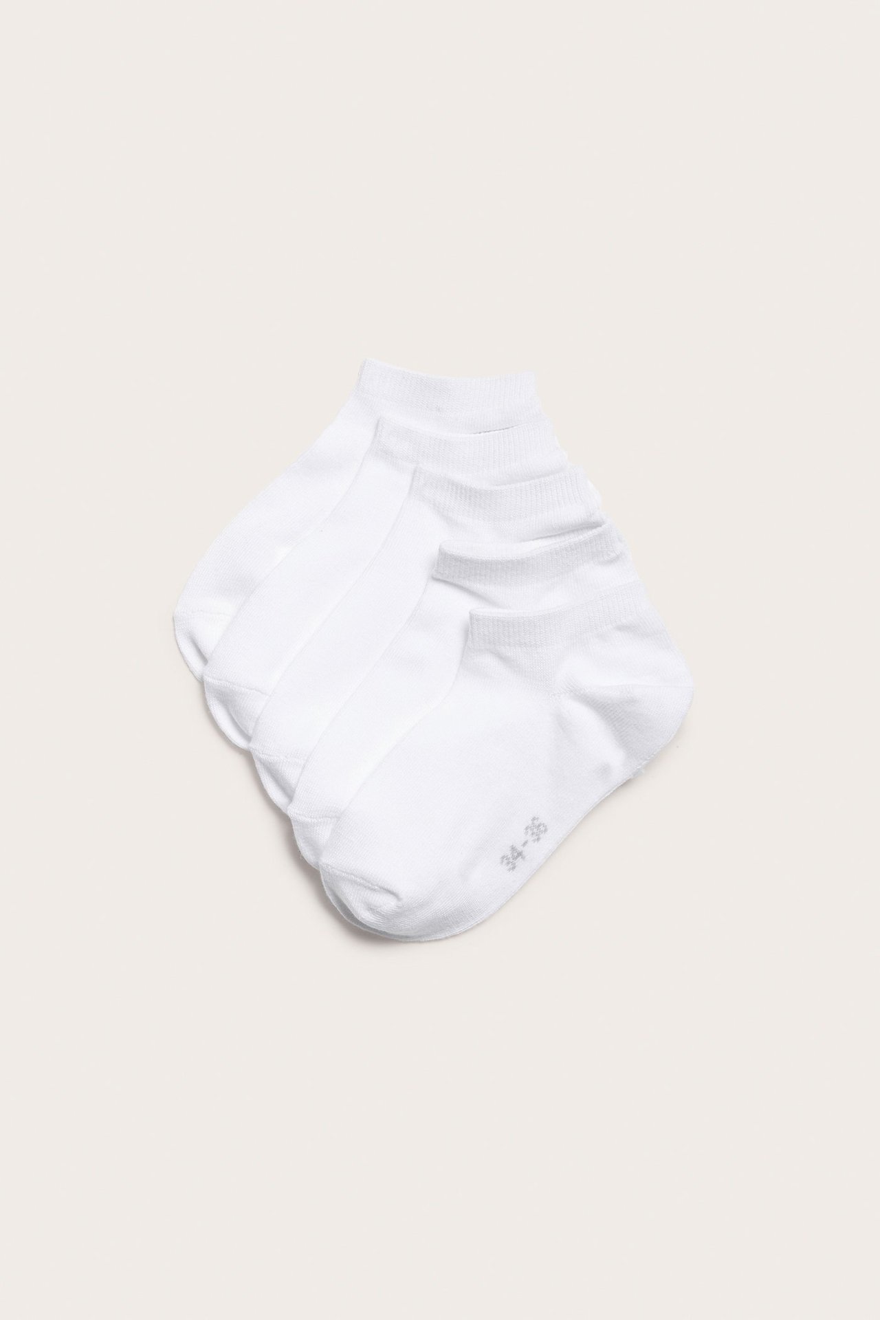 Ylhäältä kuvattuna viisi paria valkoisia nilkkasukkia puuvillasekoituksesta, vinottain pinottuna.