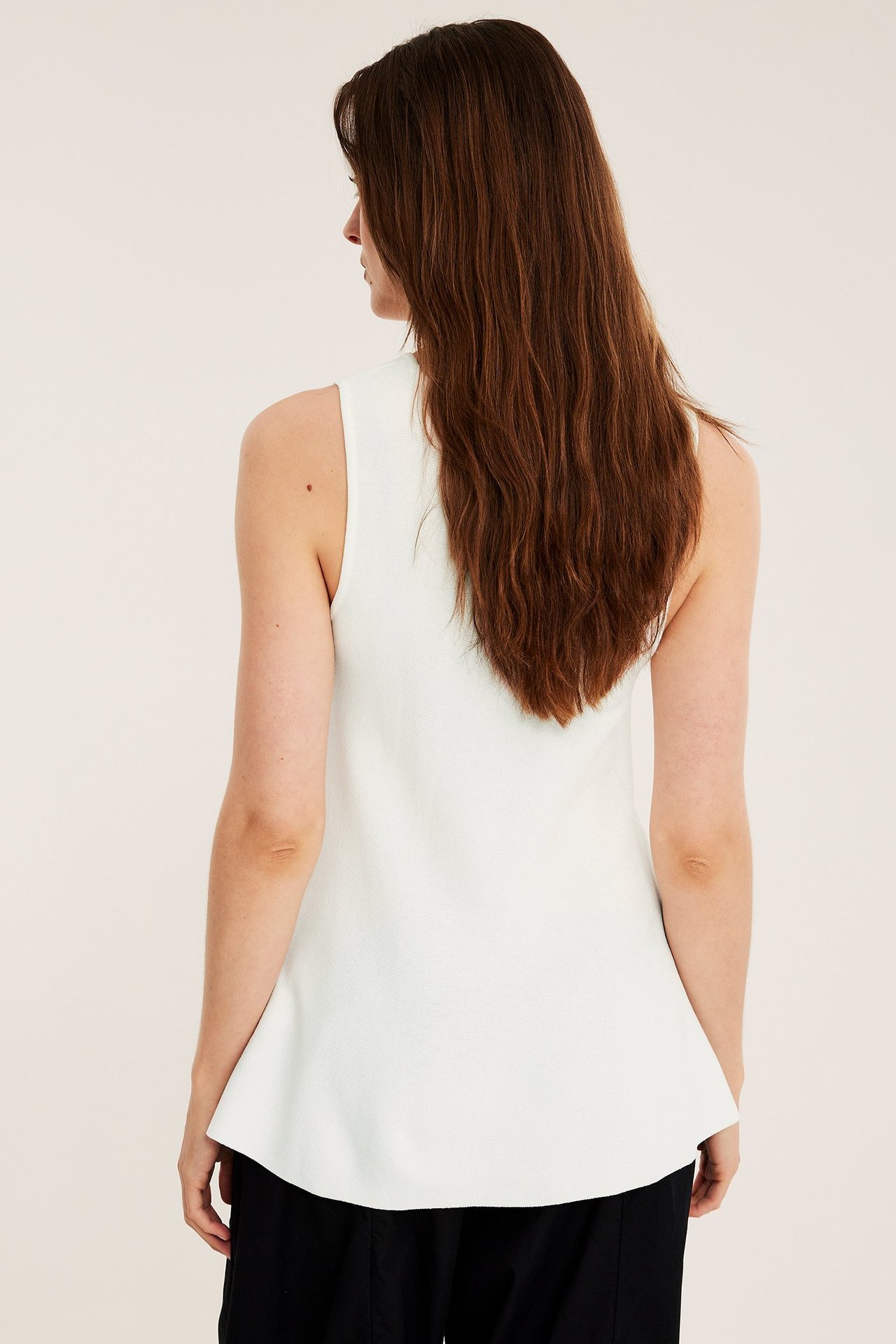 Bakifrån, kvinna i offwhite stickad peplumtopp och svarta byxor.