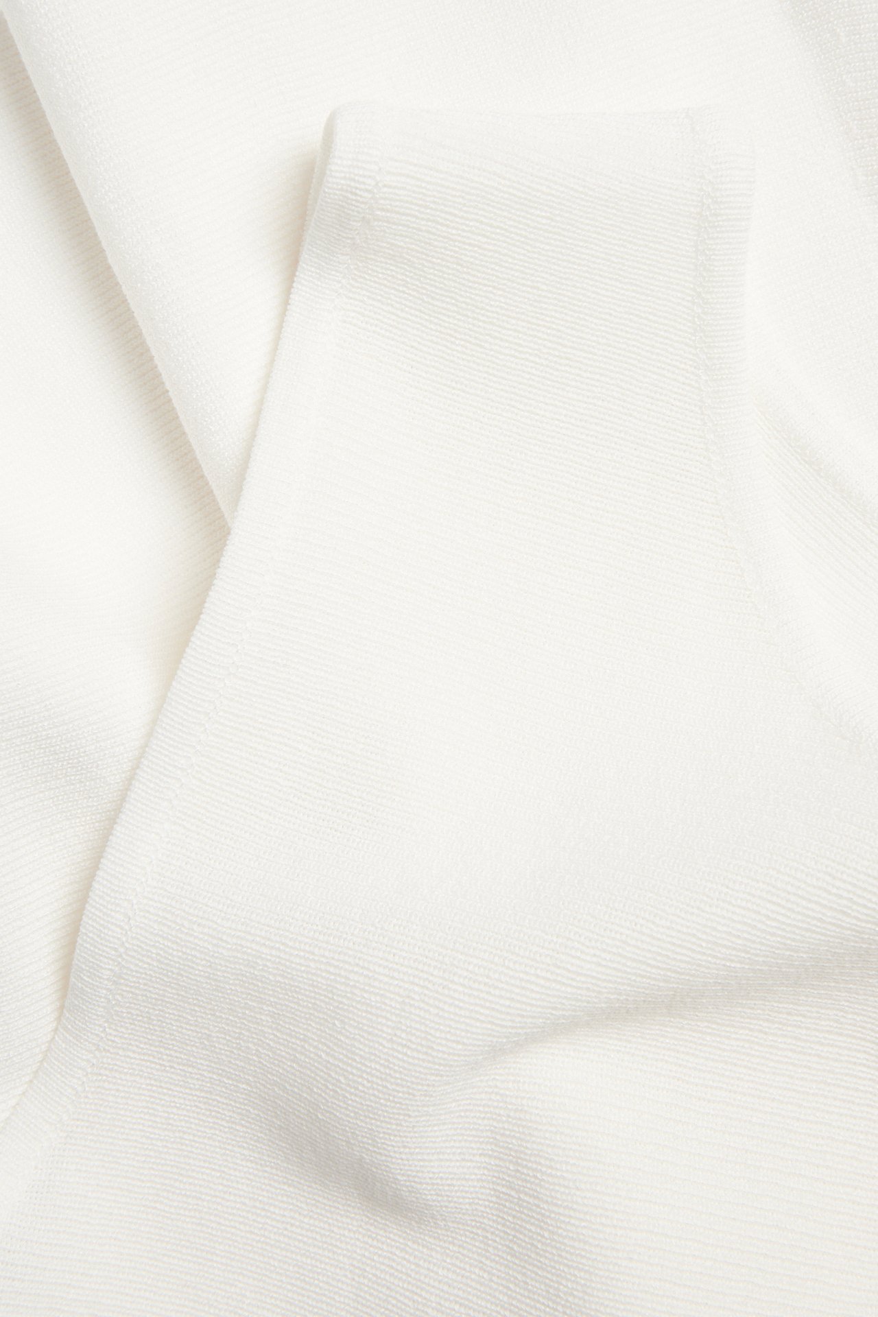 Zbliżenie na dzianinowy top peplum w kolorze off-white z wiskozy z delikatnym prążkowanym splotem.
