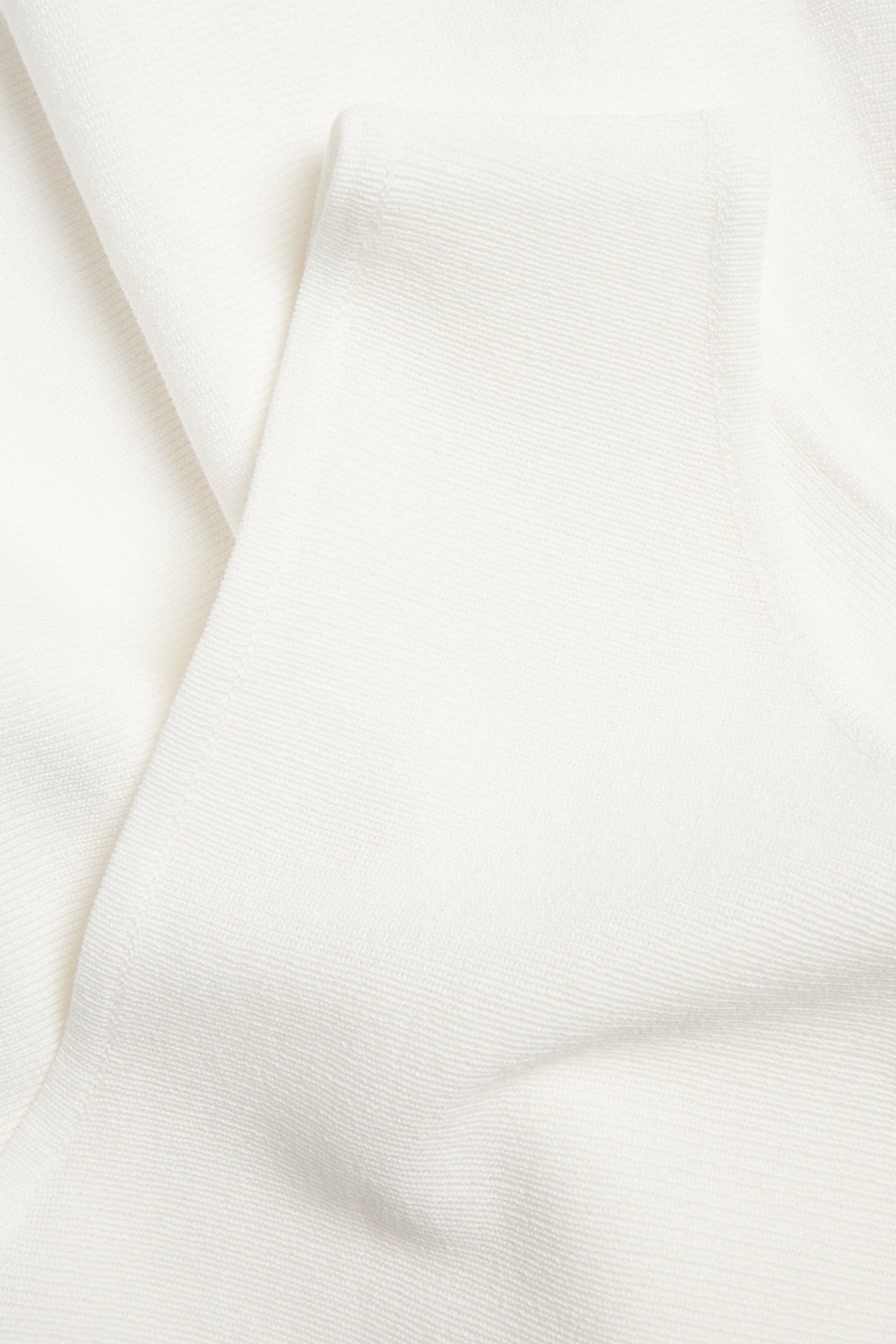 Zbliżenie na dzianinowy top peplum w kolorze off-white z wiskozy z delikatnym prążkowanym splotem.