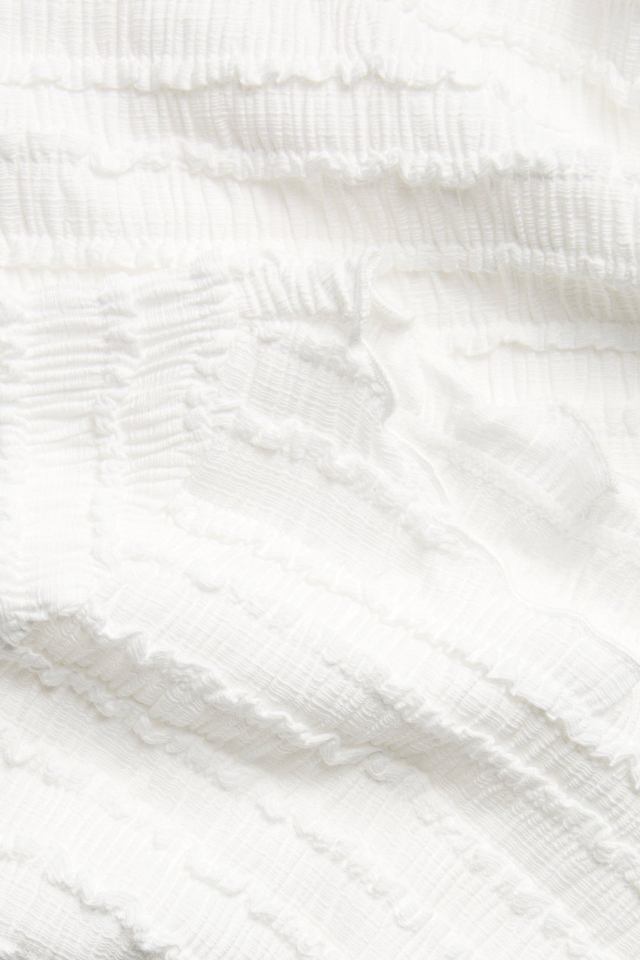 Zbliżenie na kremowy, teksturowany materiał z delikatnie pogniecioną powierzchnią, z topu z dekoltem łódkowym.