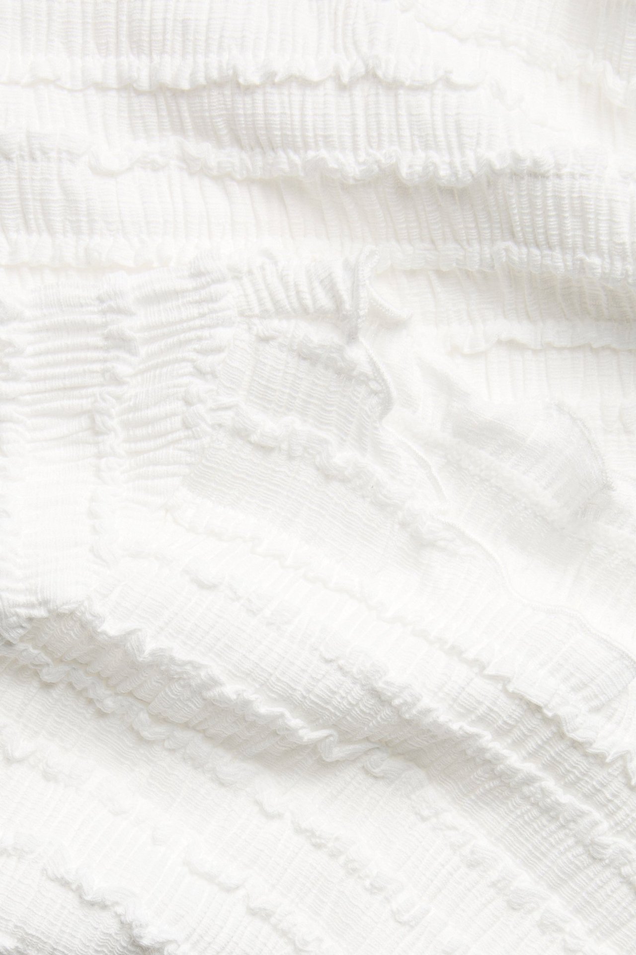 Närbild av offwhite strukturerat tyg med en subtilt skrynklig yta, från en båtringad topp.