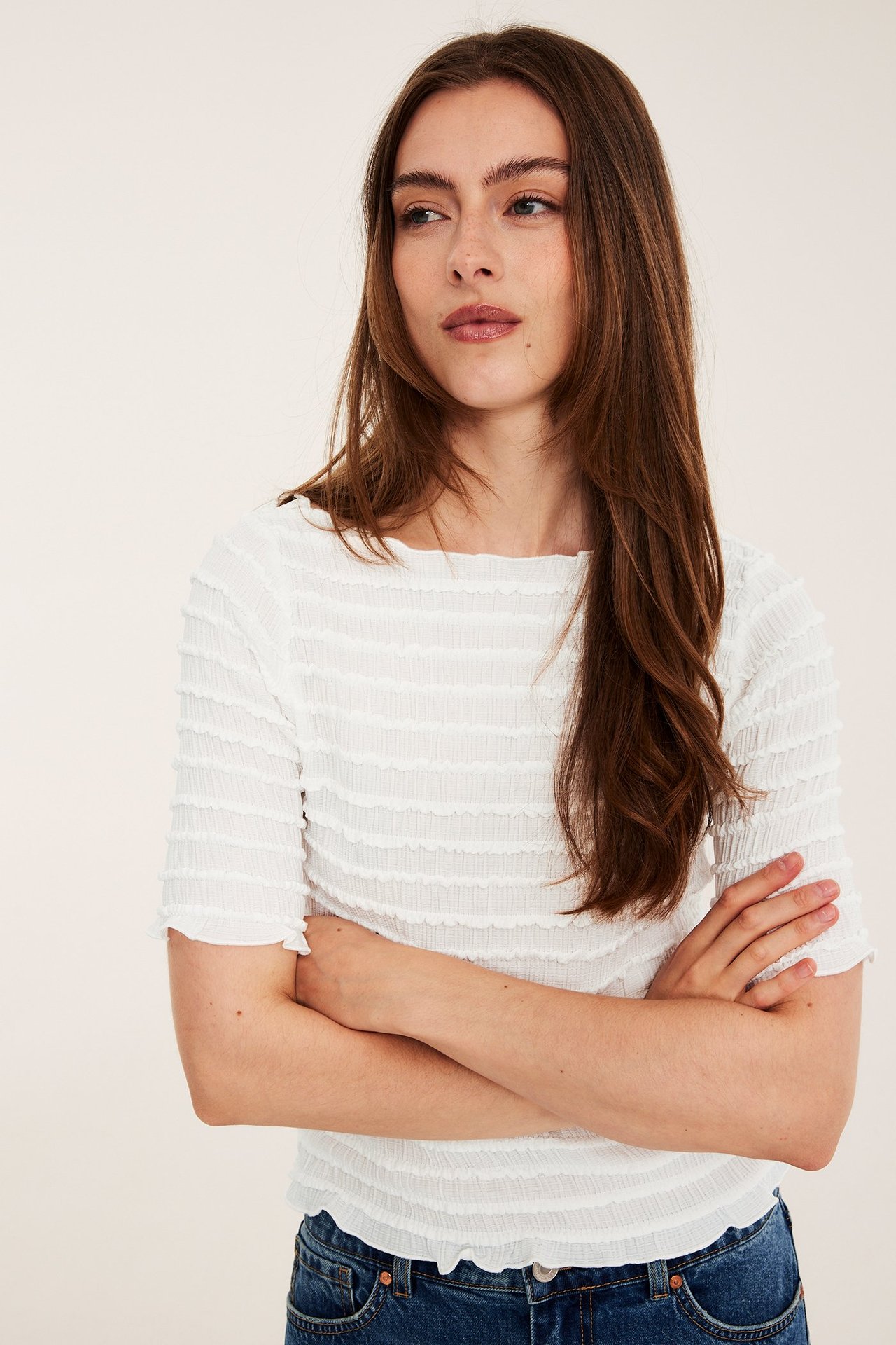 Edestäpäin nainen yllään luonnonvalkoinen kuvioitu venekaula-aukollinen toppi ja siniset farkut.