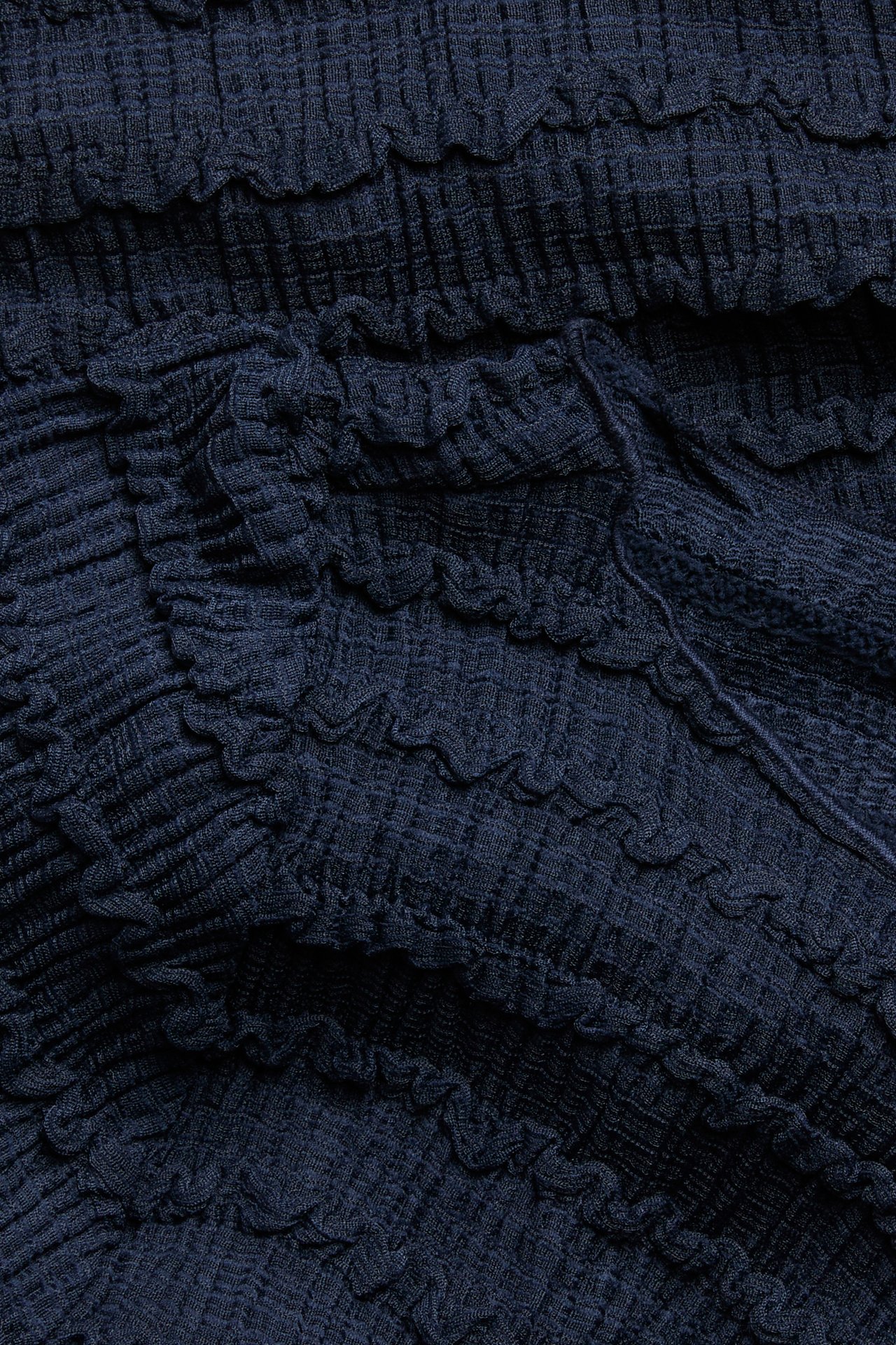 Zbliżenie ciemnoniebieskiej tkaniny topu z fakturą, pokazujące marszczone i faliste detale.