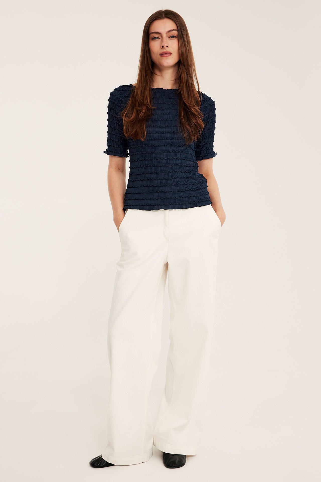 Kobieta w ciemnoniebieskim teksturowanym topie, szerokich beżowych spodniach i czarnych butach, przód.