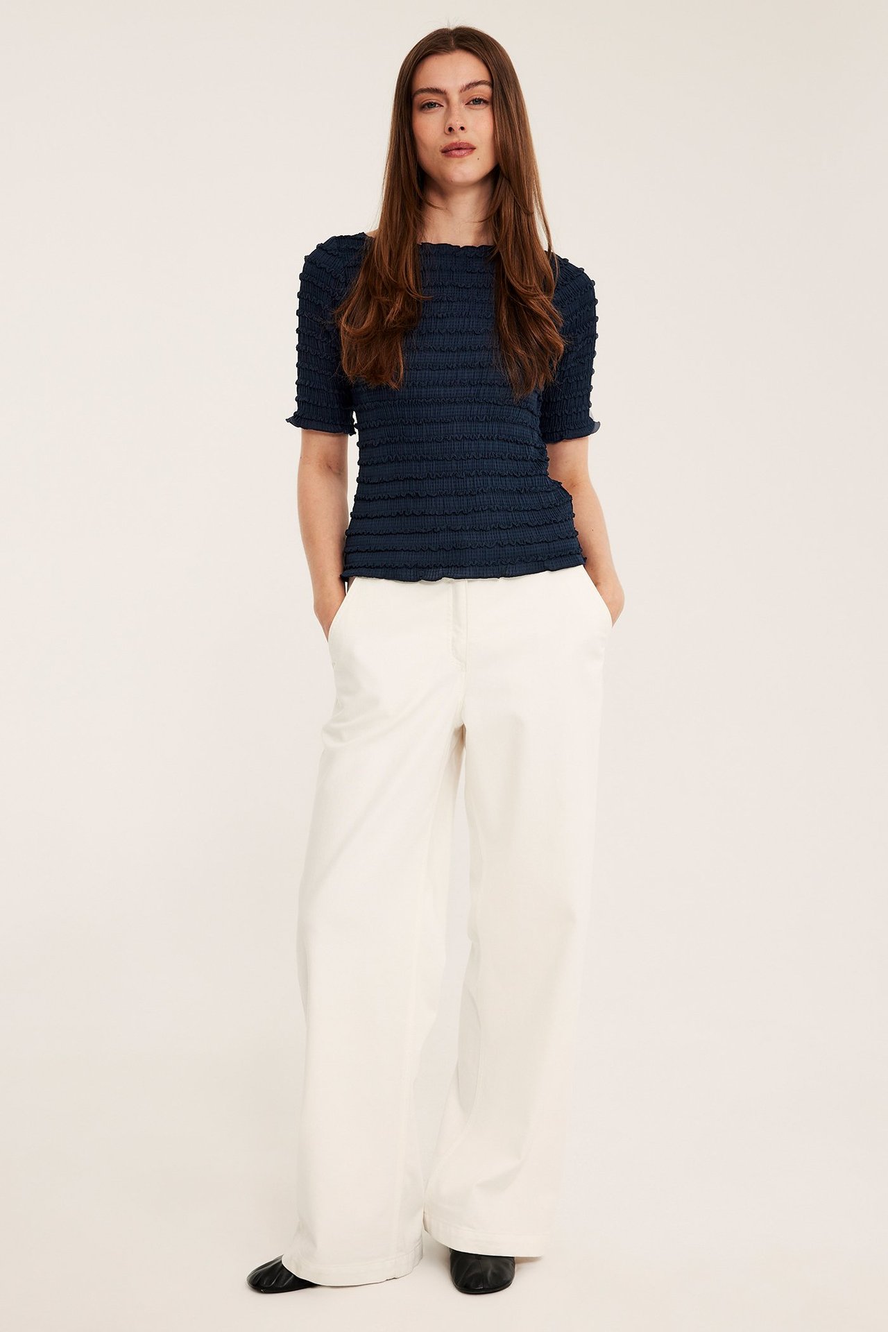 Kobieta w ciemnoniebieskim teksturowanym topie, szerokich beżowych spodniach i czarnych butach, przód.