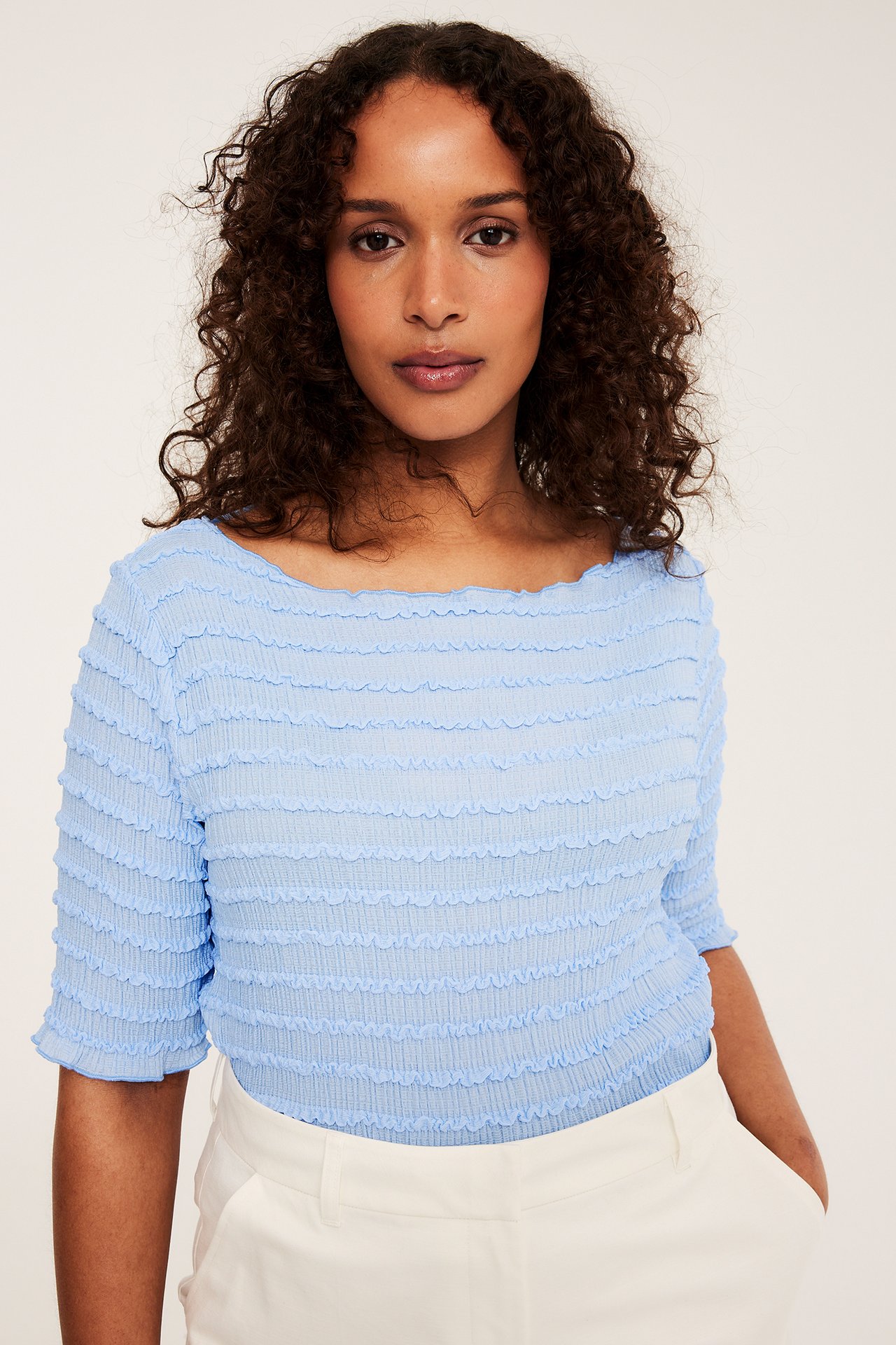 Framifrån, kvinna i ljusblå strukturerad topp med båtringning, korta ärmar och vita byxor.