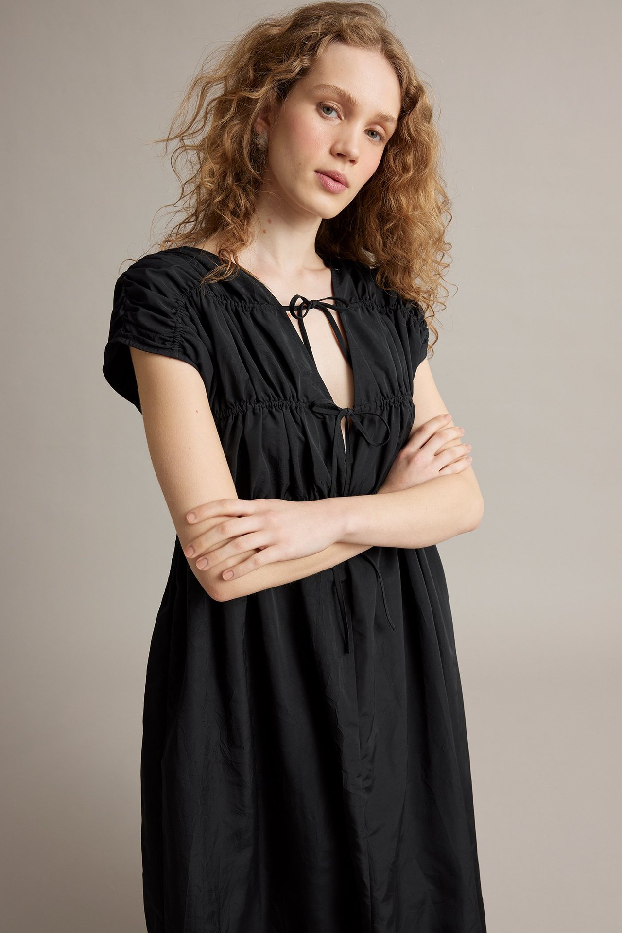 Edestä, nainen mustassa strukturoidussa maksimekossa V-pääntien solmuilla ja lyhyillä rypytetyillä hihoilla.