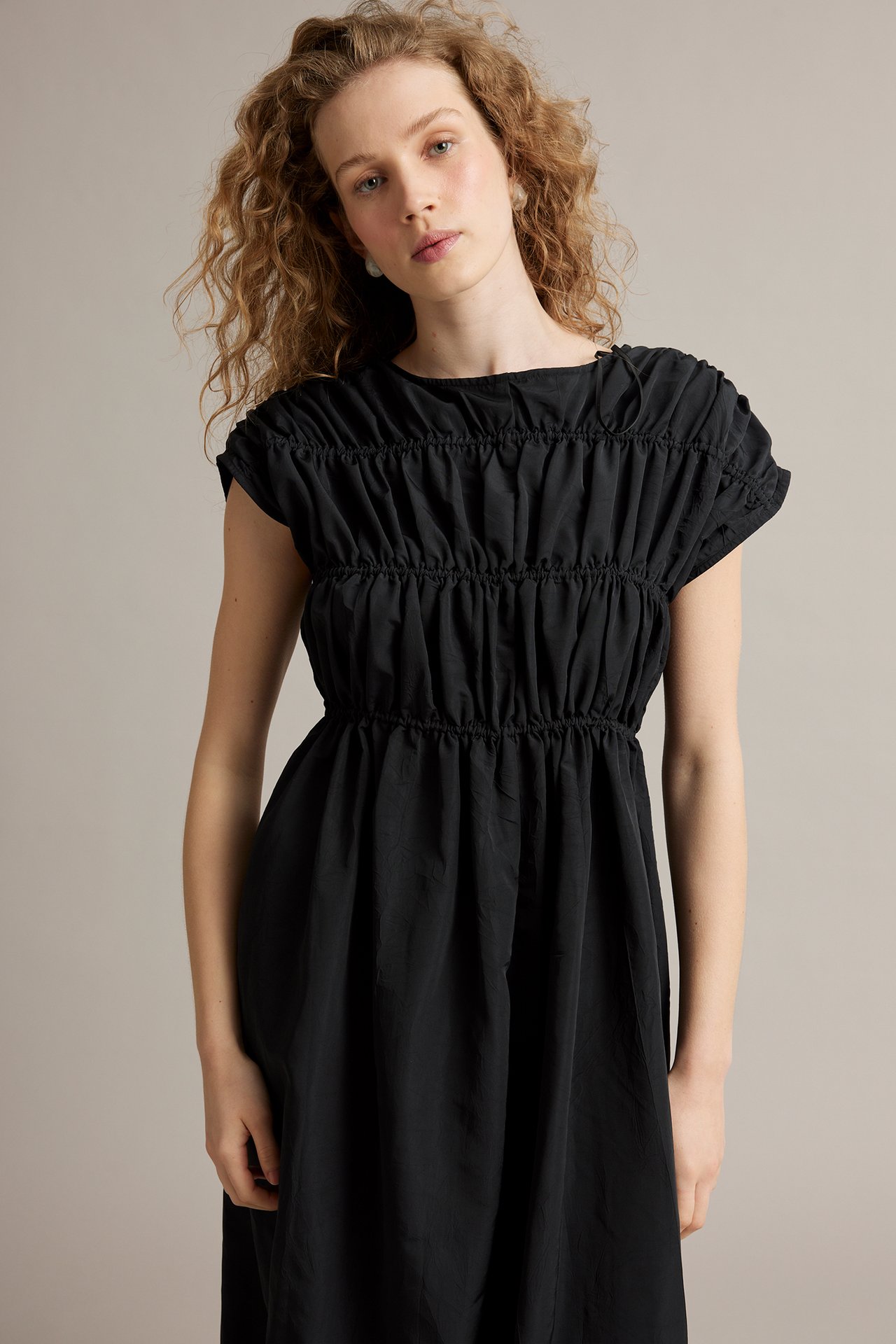 Edestä kuvattu nainen yllään musta strukturoitu pitkä mekko, jossa rypytetty yläosa ja sidontanauhat.