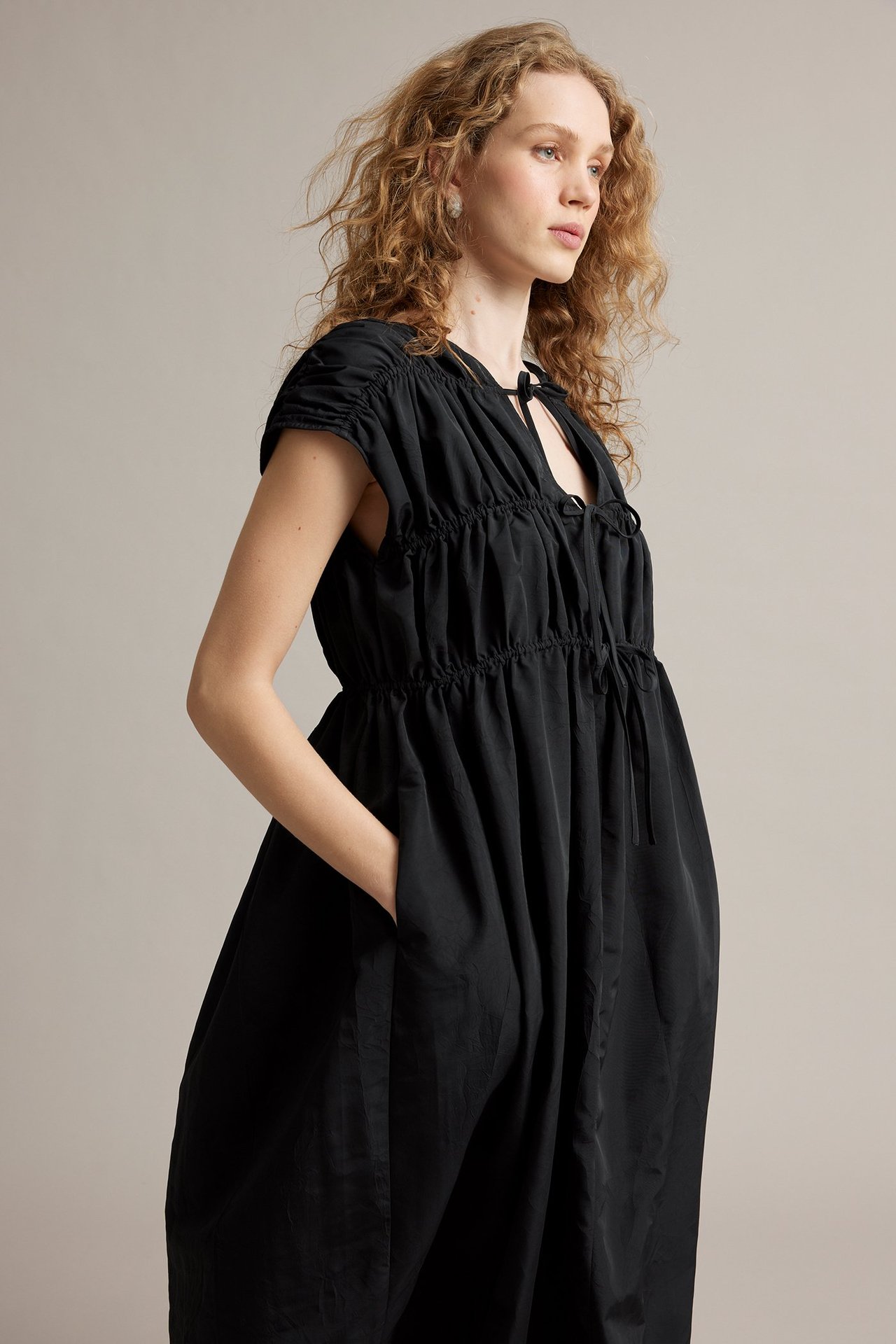 Widok z przodu: kobieta w czarnej sukience poliestrowej z wiązaniami, marszczoną górą i kieszeniami.