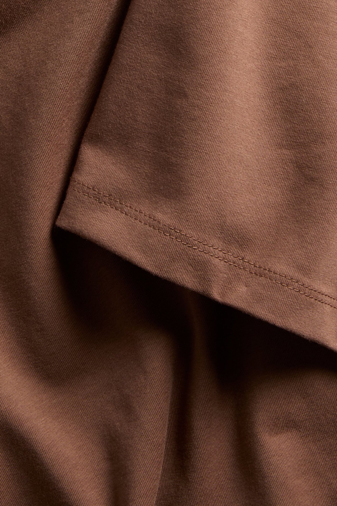 Zbliżenie na brązowy, dopasowany t-shirt z mieszanki bawełny, ukazujące teksturę materiału i obszycie.