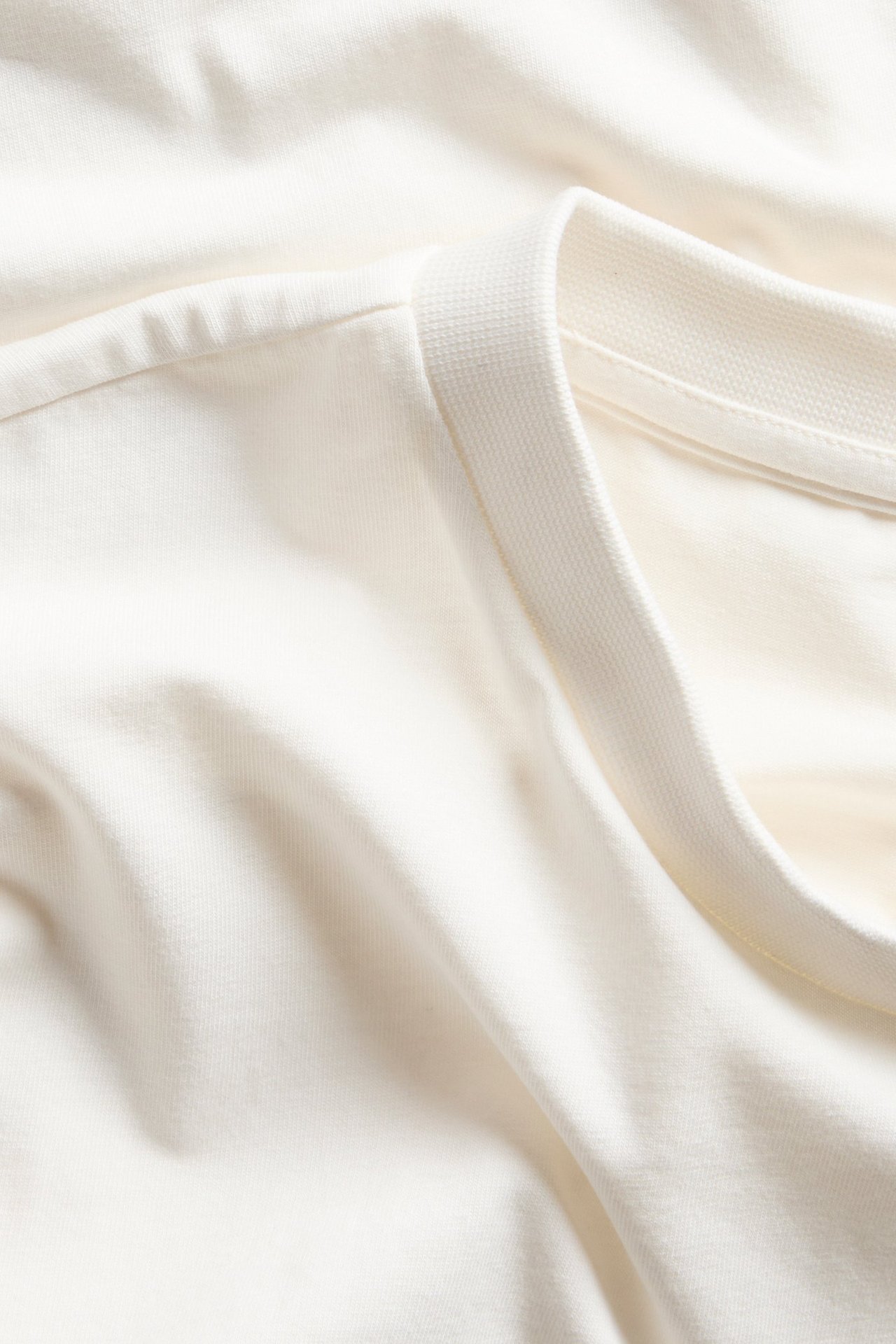 Zbliżenie na białawy, dopasowany t-shirt z prążkowanym dekoltem i obniżonymi ramionami.