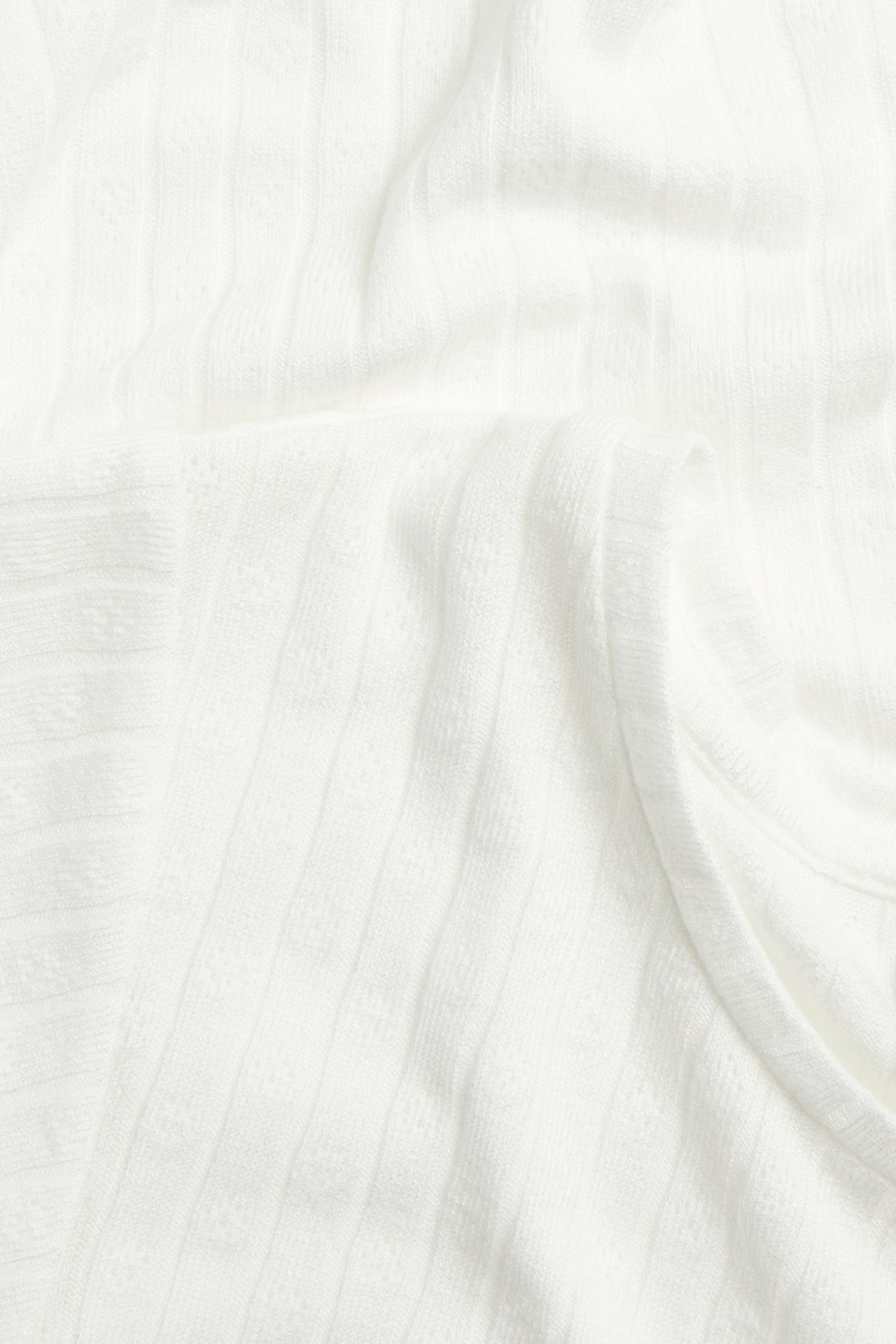 Nærbilde av et offwhite ribbet pointelle-toppstoff med diskret mønster.