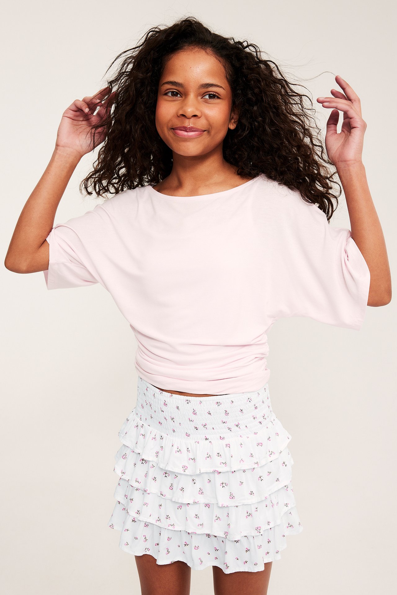 Etunäkymä: Lapsi valkoisessa kukkakuvioisessa kerroshameessa smock-vyötäröllä ja vaaleanpunainen toppi.