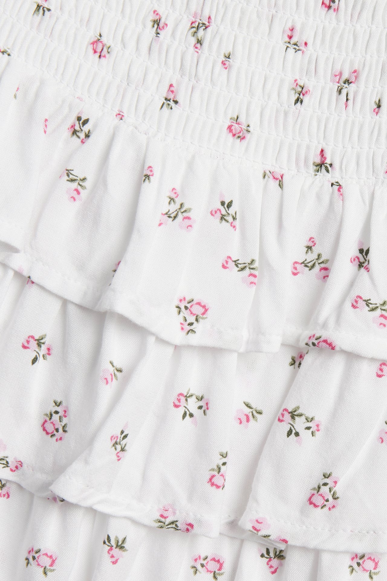 Närbild av vit viskoskjol med smockad midja och rosa blommönster, med volanger.