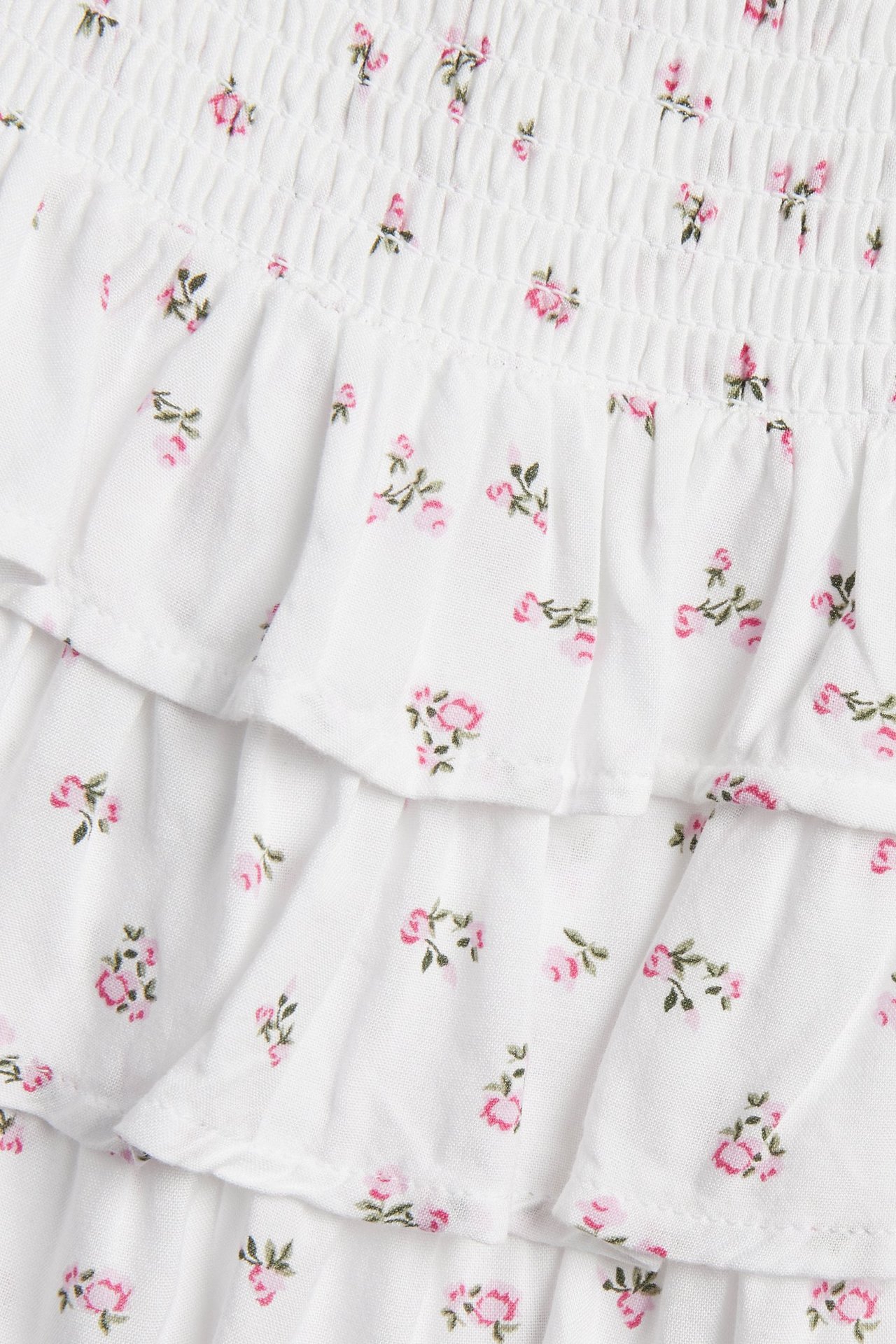 Närbild av vit viskoskjol med smockad midja och rosa blommönster, med volanger.