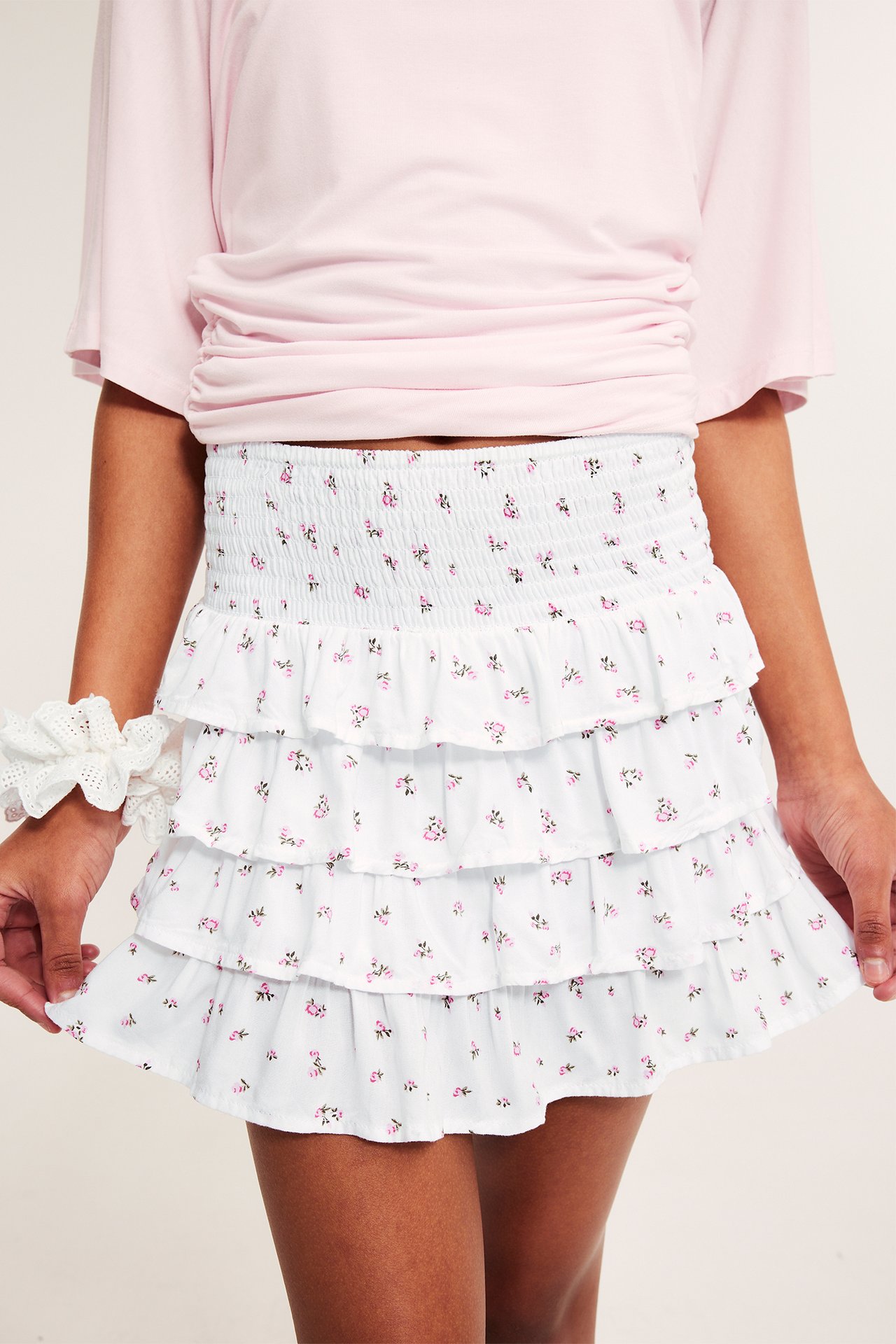 Edestä: Lapsi valkoisessa viskoosihameessa, jossa vaaleanpunainen kukkakuvio, vaaleanpunainen toppi ja valkoinen scrunchie.